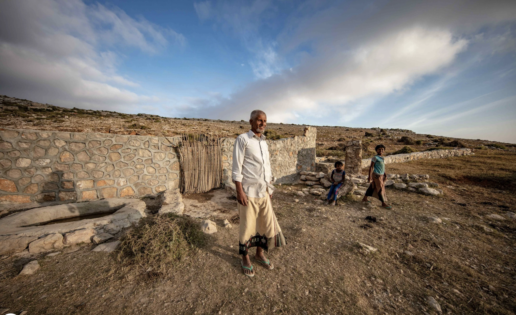 一名男子站在一个雨水蓄水池附近，两个孩子站在他身边。