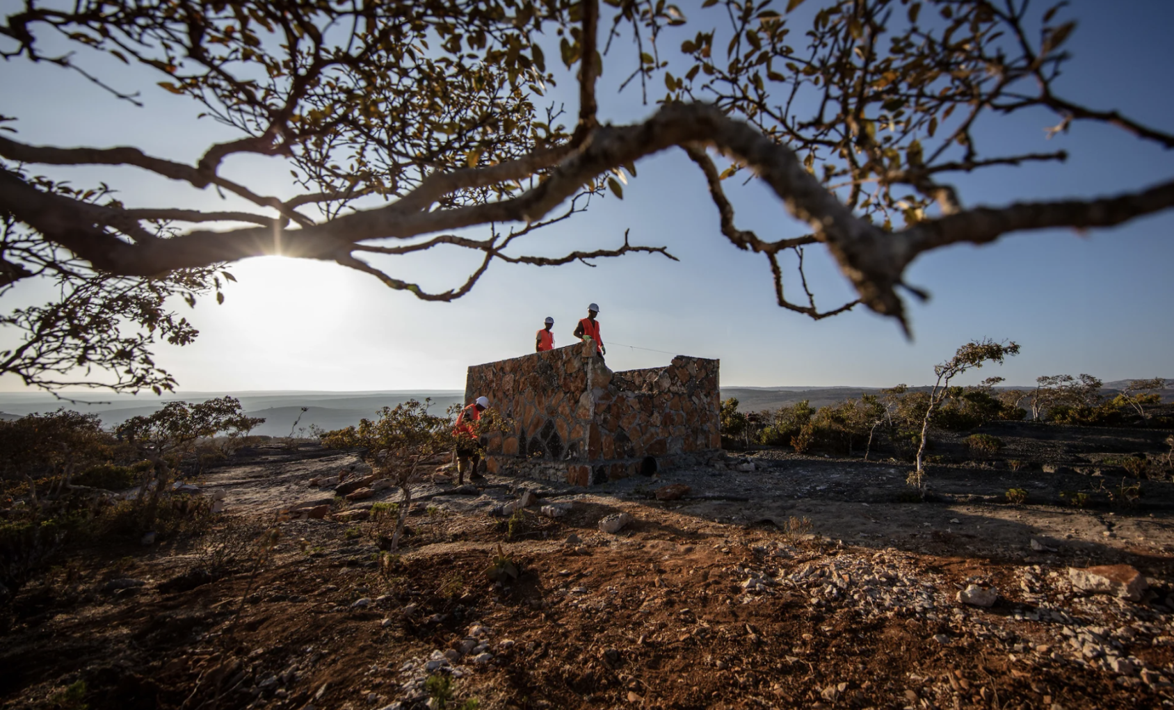 三个建筑工人站在一个方形的砖块结构上。