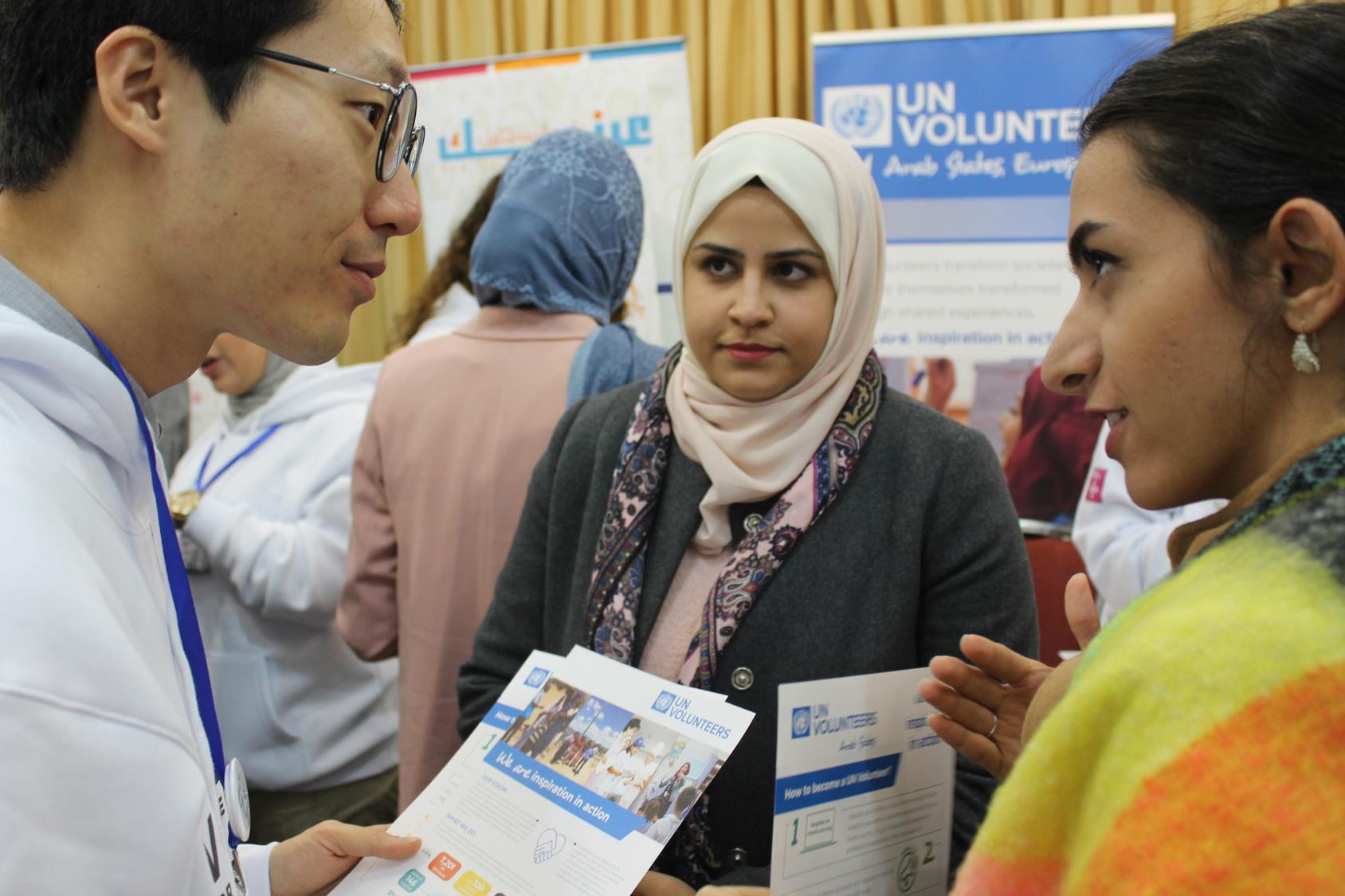 Three people, holding pamphlets, speak to each other. 