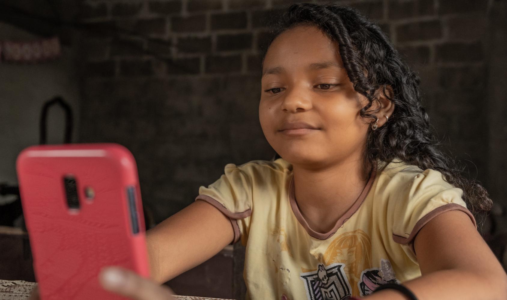 Se muestra a una chica joven observando concentrada la pantalla de un teléfono móvil.