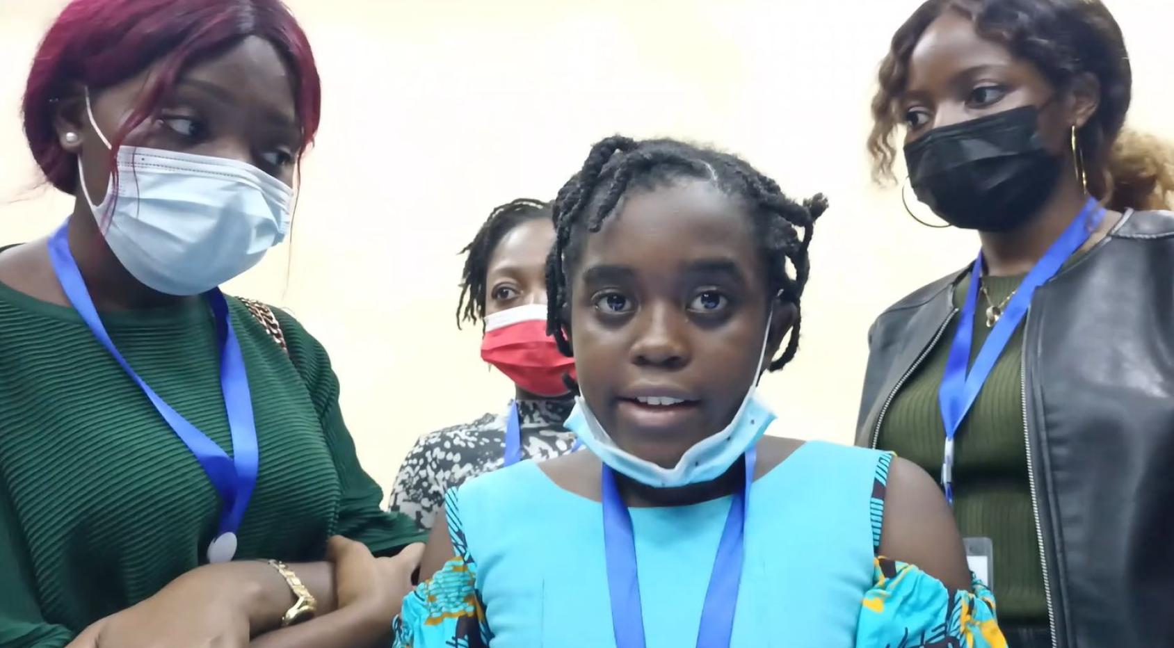 Una joven con camisa azul claro mira directamente a la cámara y está rodeada por otras tres mujeres.