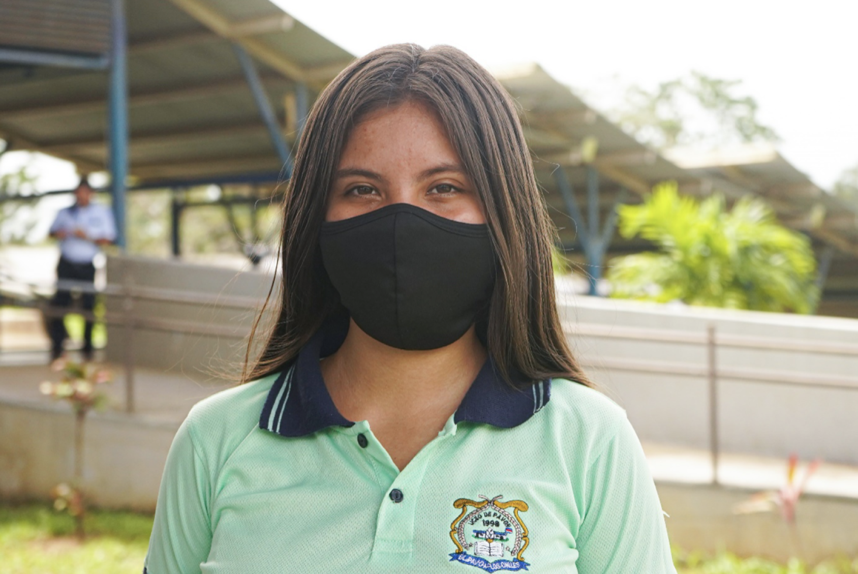 Una niña con uniforme escolar y mascarilla negra mira directamente a la cámara en su escuela.