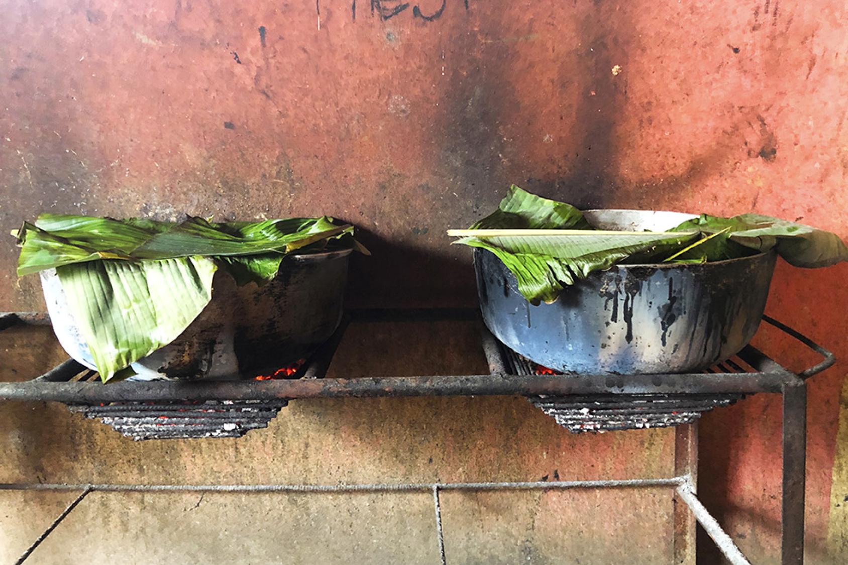 两口锅放在火上，上面放着香蕉叶。