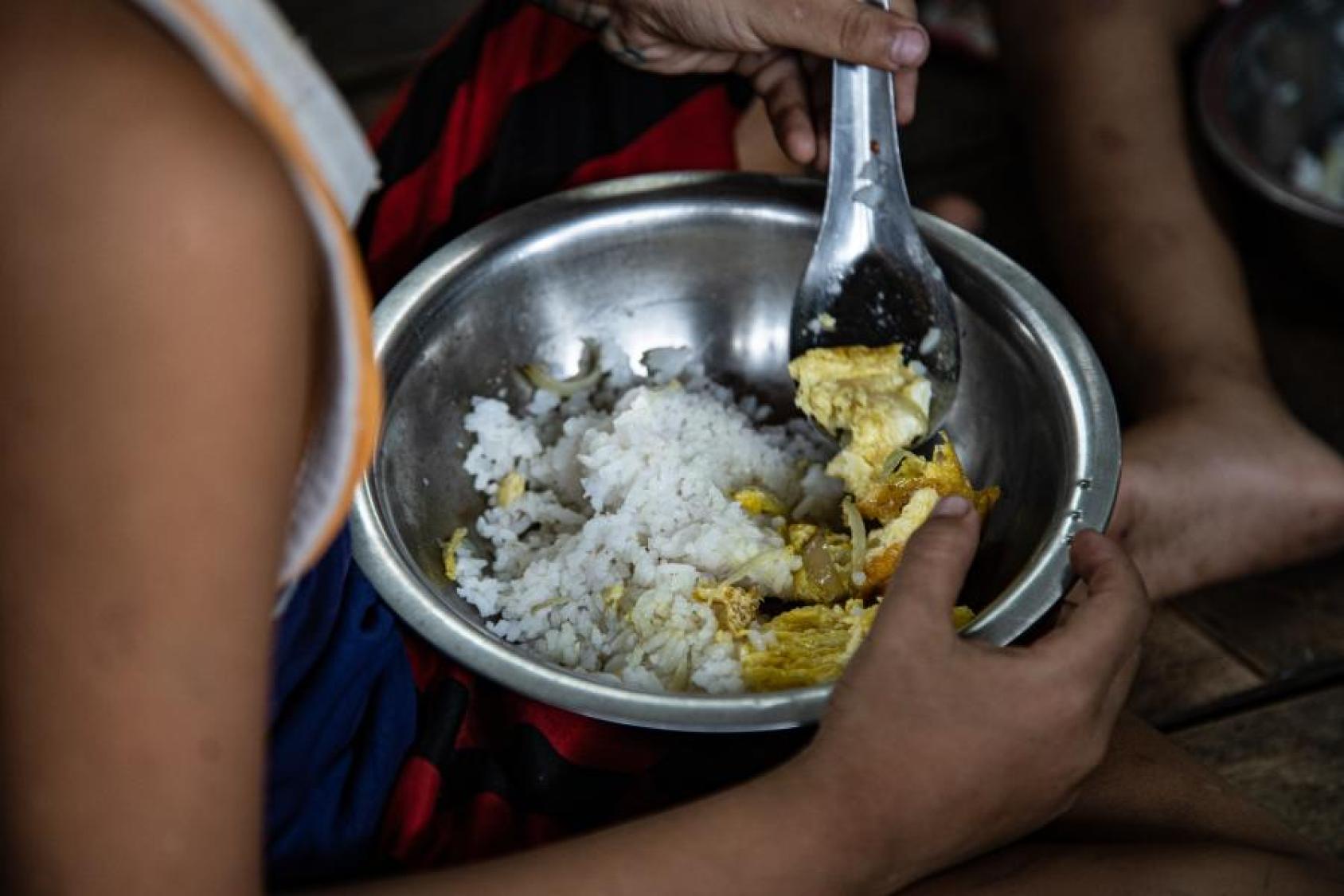 A child holding a plateful of rice and eggs.