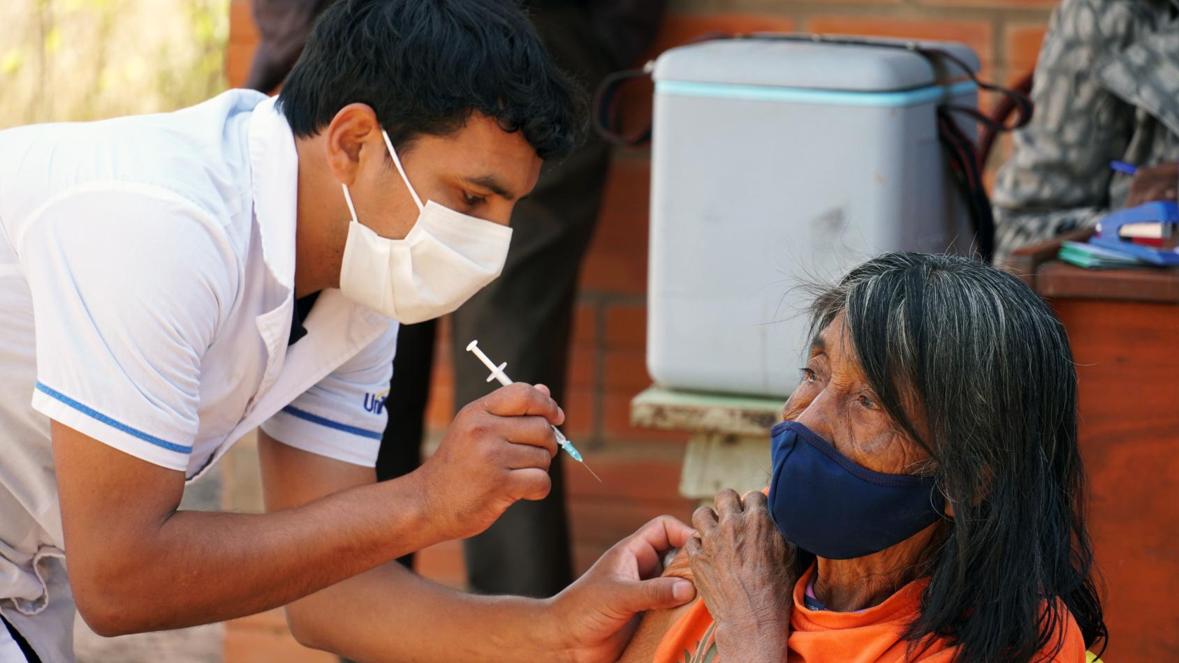 A woman rolls up her sleeve a as a man administers a Covid-19 vaccination in her arm. 