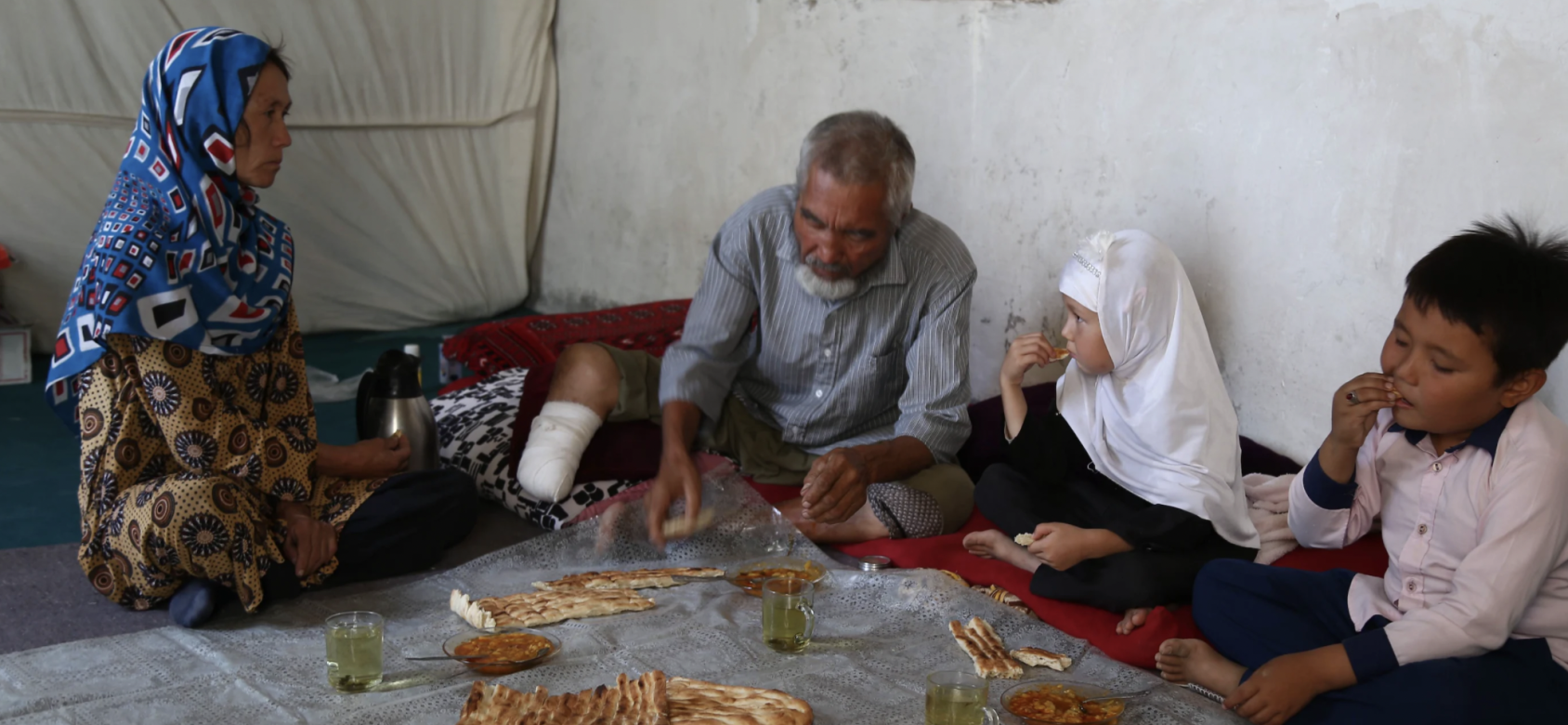 A family of four have a meal together on the ground. 