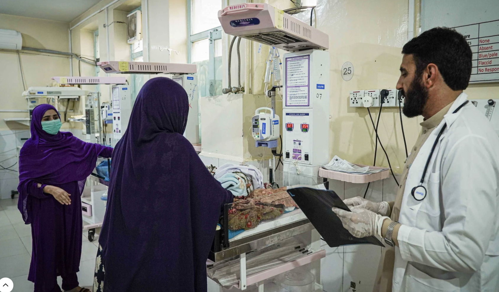 Three health care workers stand near newborn cribs. 