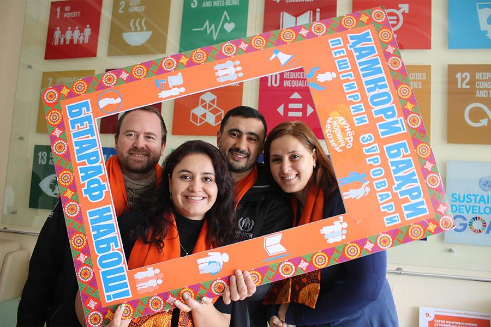 Four people smile at the camera while holding an orange sign around them. 