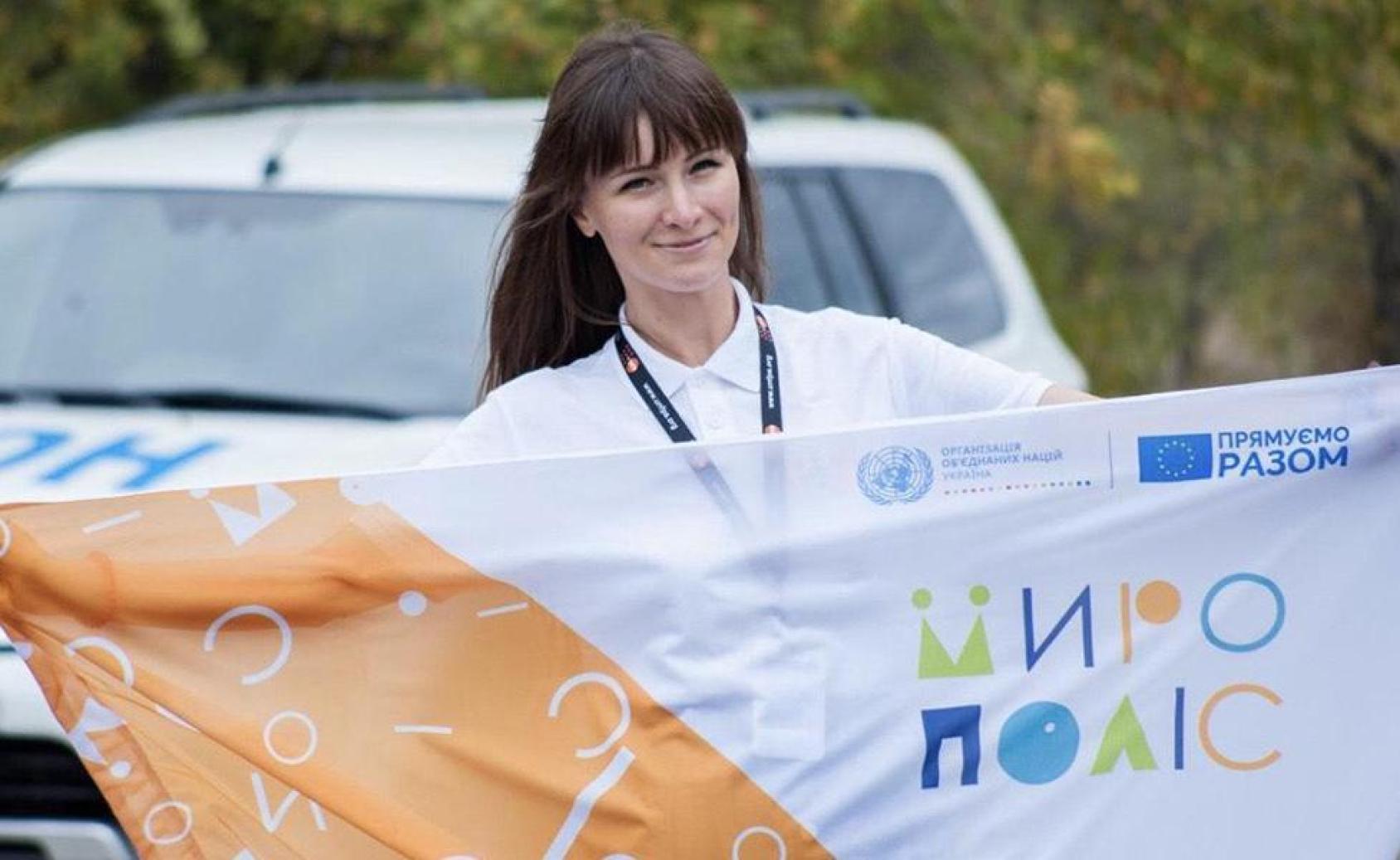 A woman, with her arms out, holds a white and orange flag with words on it. 