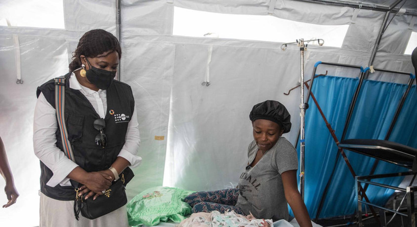 La Directora Ejecutiva Adjunta del UNFPA, Diene Keita, se encuentra junto a una madre que está sentada en una cama junto a su nuevo bebé.