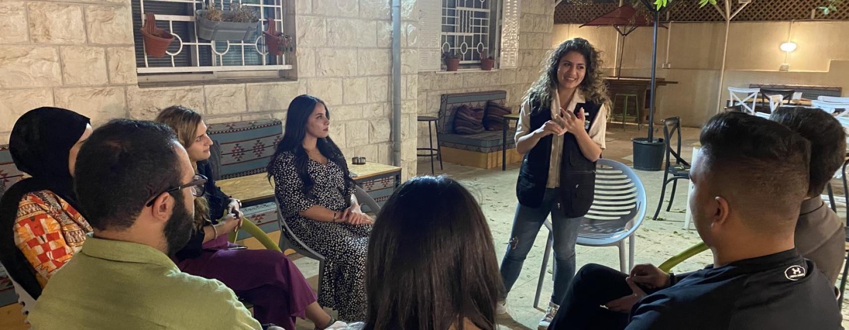 An instructor stands in the center of a group of people sitting in chairs. 