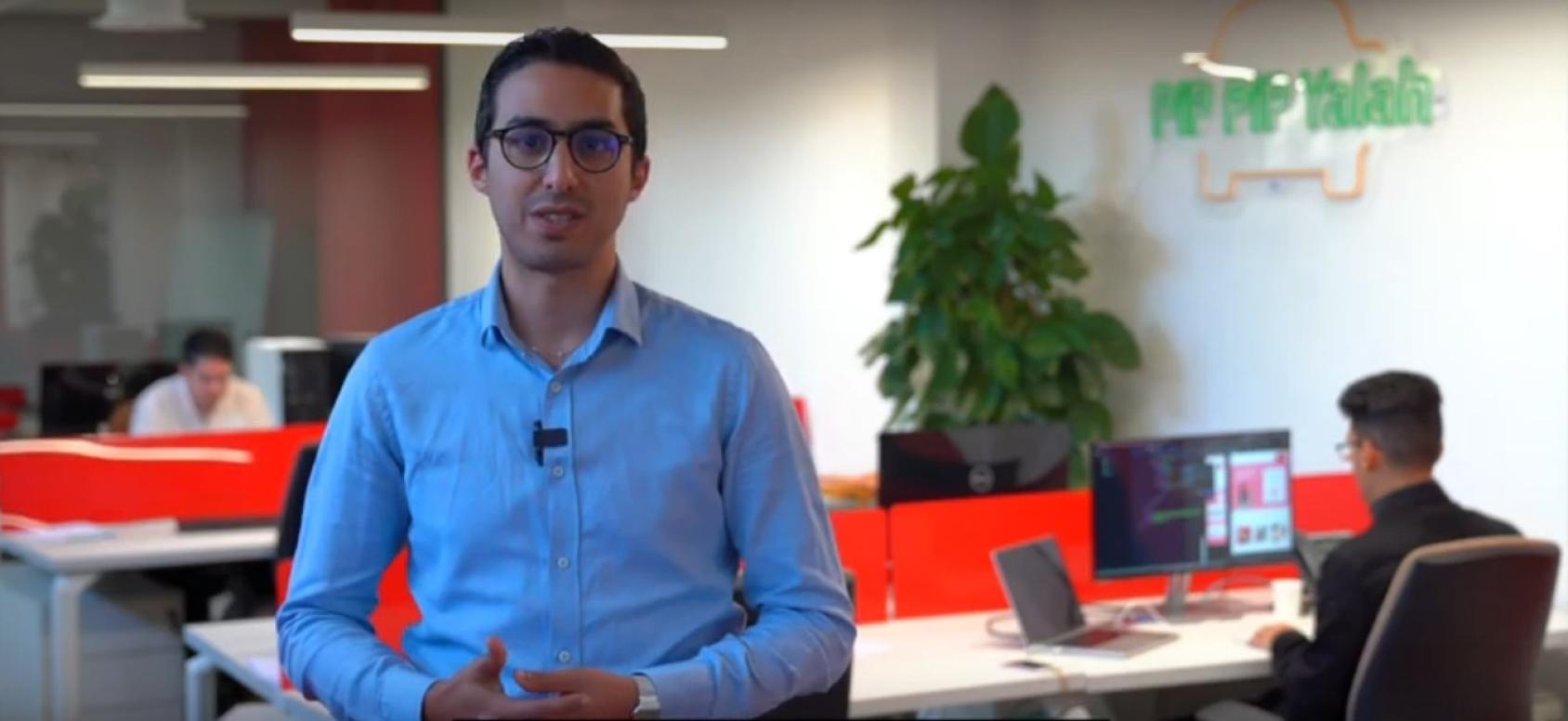 Мужчина в синей рубашке на пуговицах и черных очках смотрит прямо в камеру.