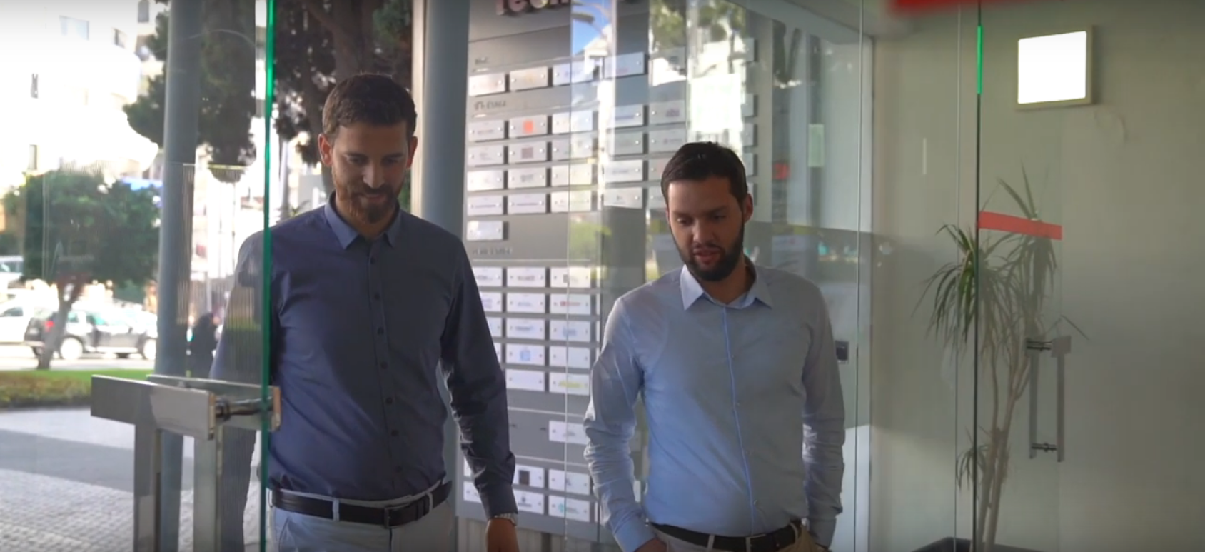 Двое мужчин в светлых рубашках проходят через стеклянную дверь. 