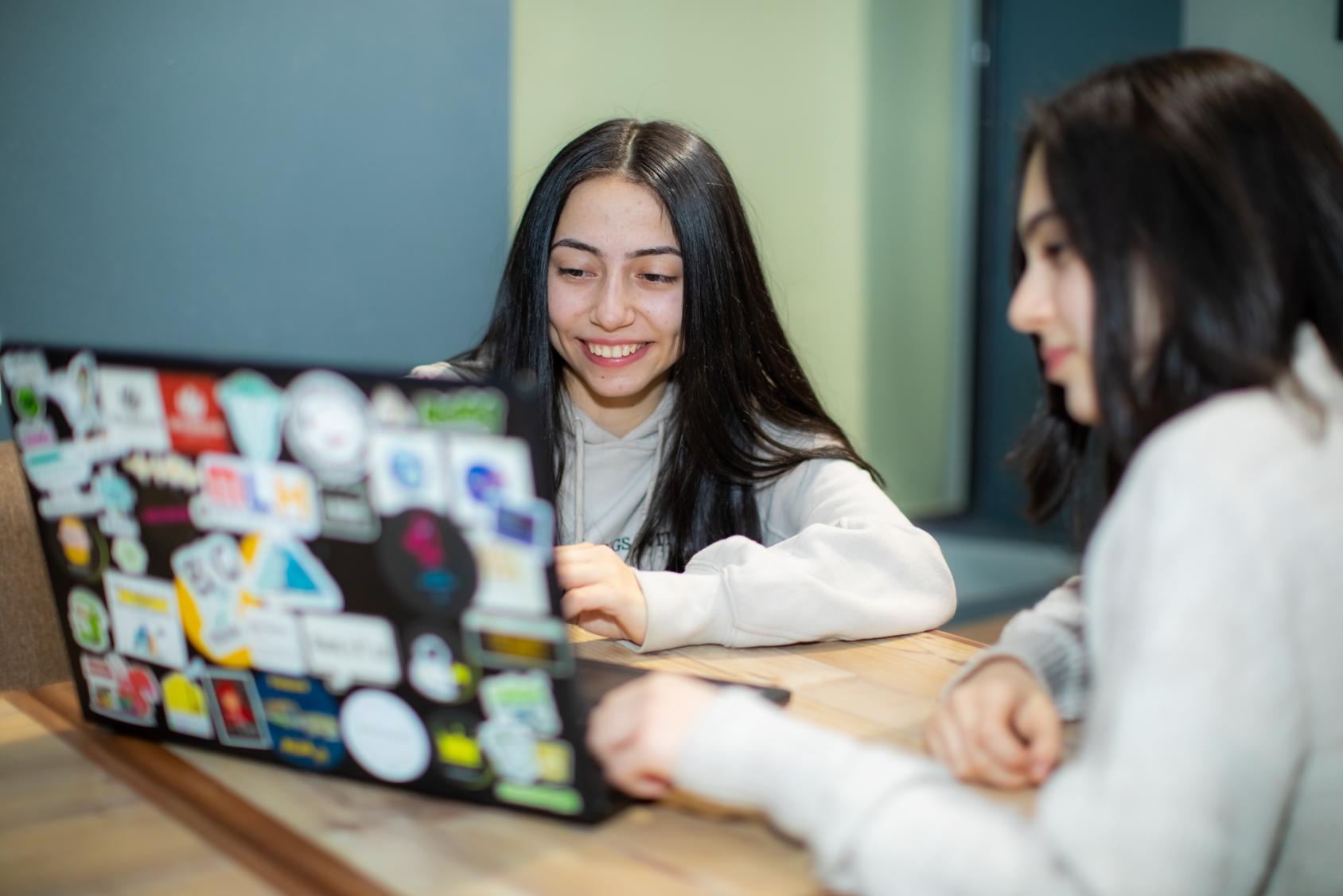 Dos niñas sentadas en un escritorio y trabajando en una computadora portátil.
