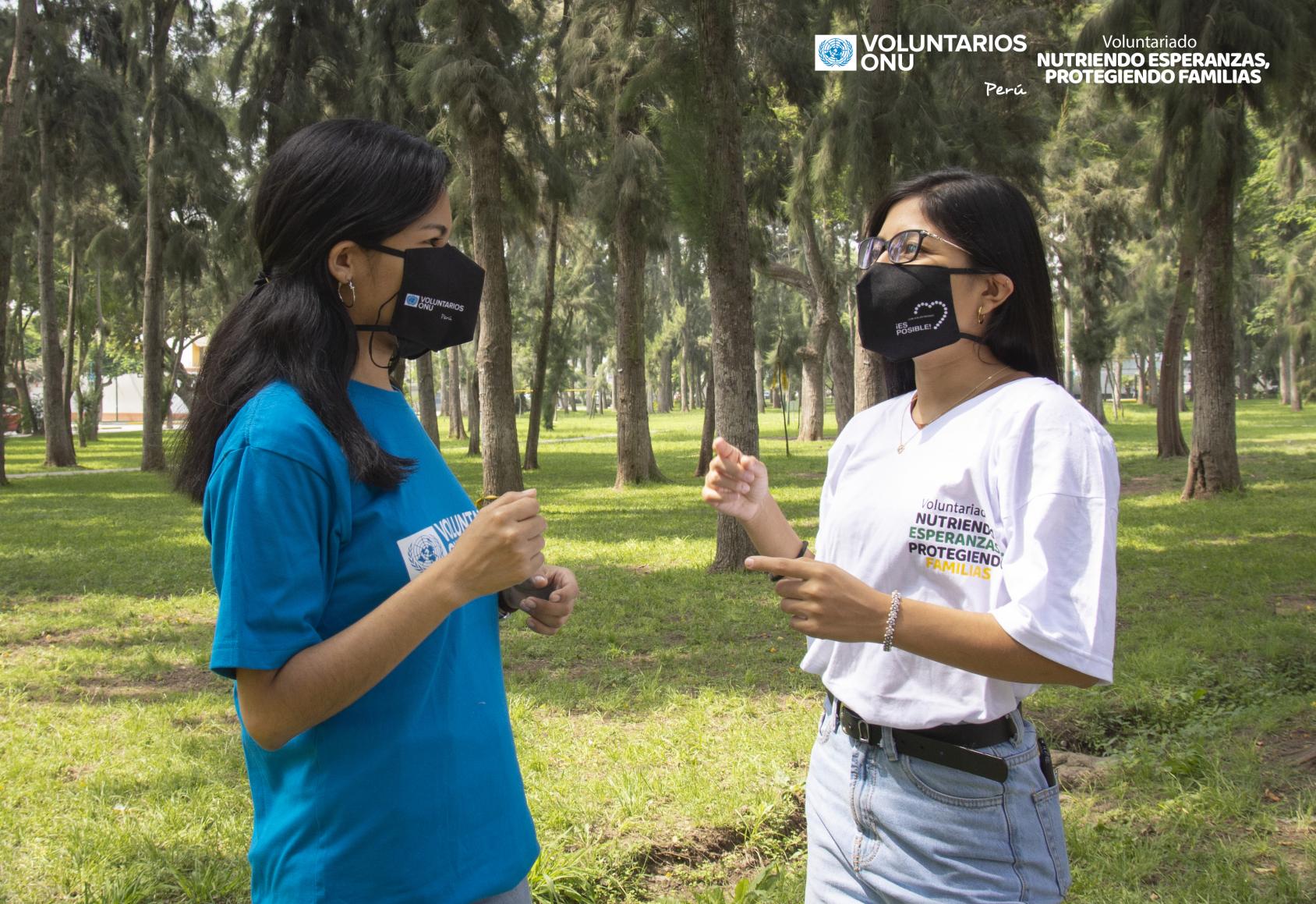 Dos chicas con mascarillas y hablando entre ellas en un jardín.