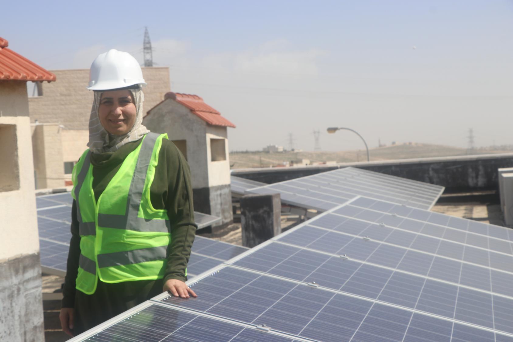 امرأة تقف بالقرب من الألواح الشمسية وتنظر مباشرة إلى الكاميرا.