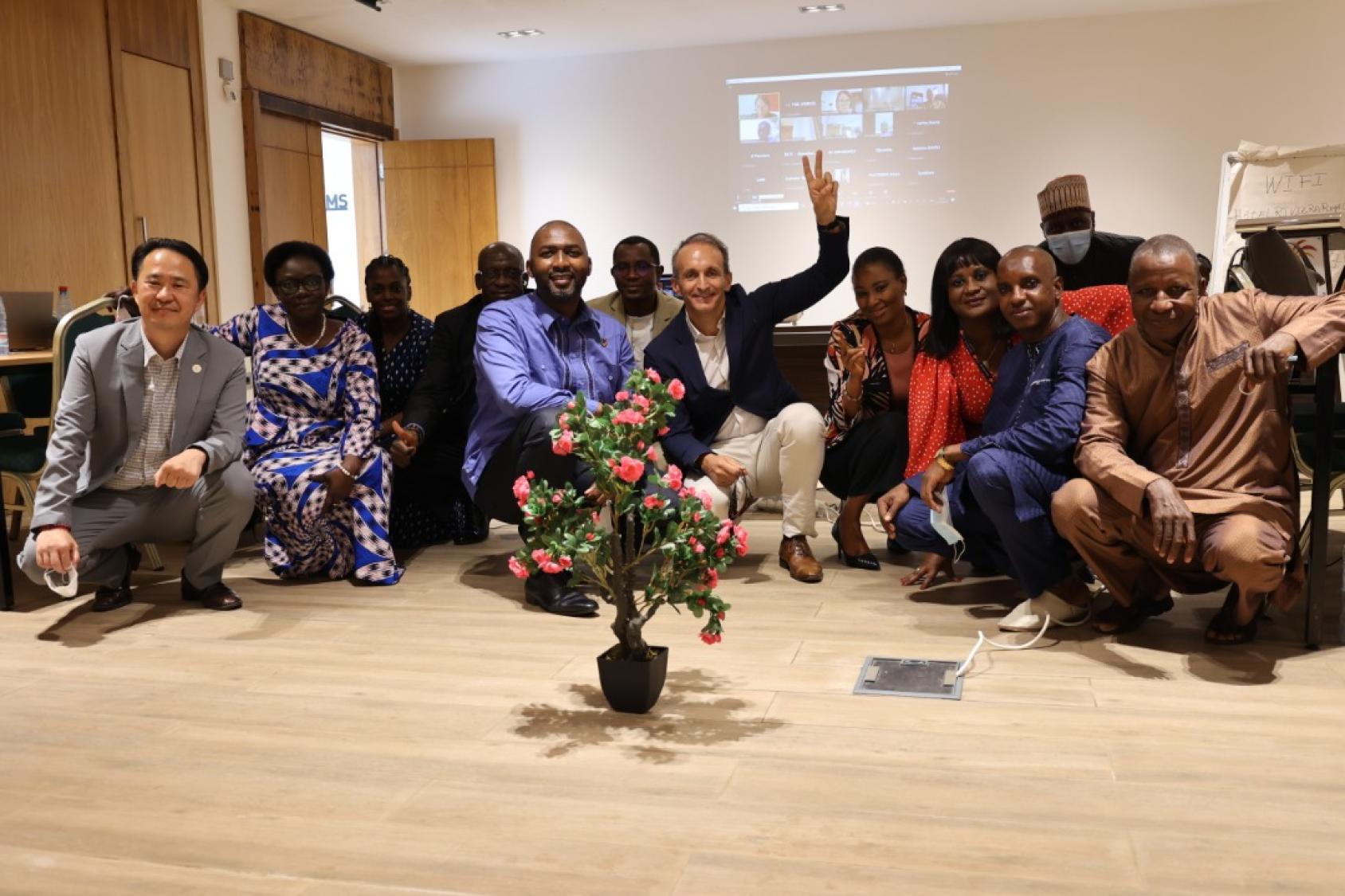 Un hombre con un traje azul que muestra el signo de la paz se sienta en el suelo con otros asistentes a un taller.