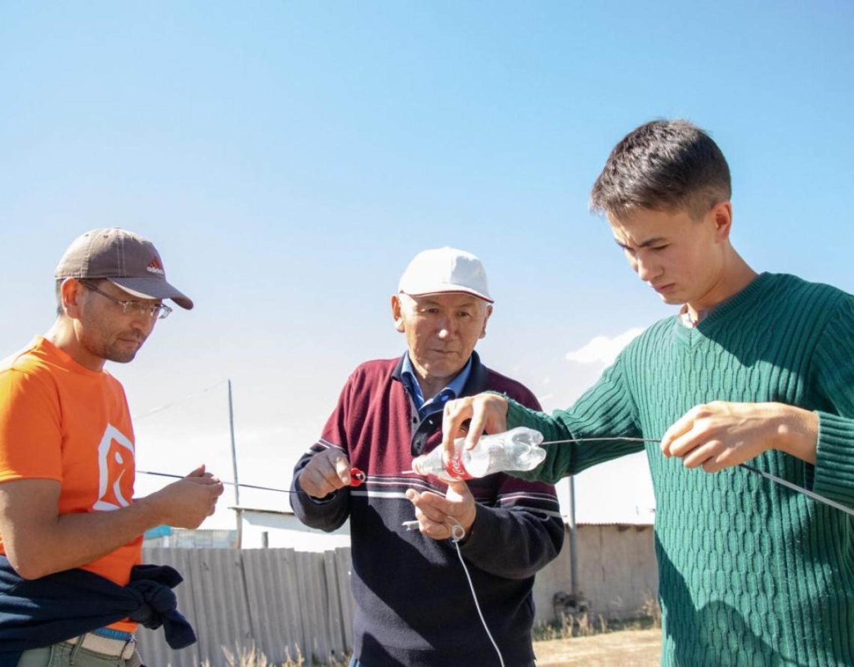 Tres hombres cubren los cables de conexión para protegerlos de las duras condiciones meteorológicas.
