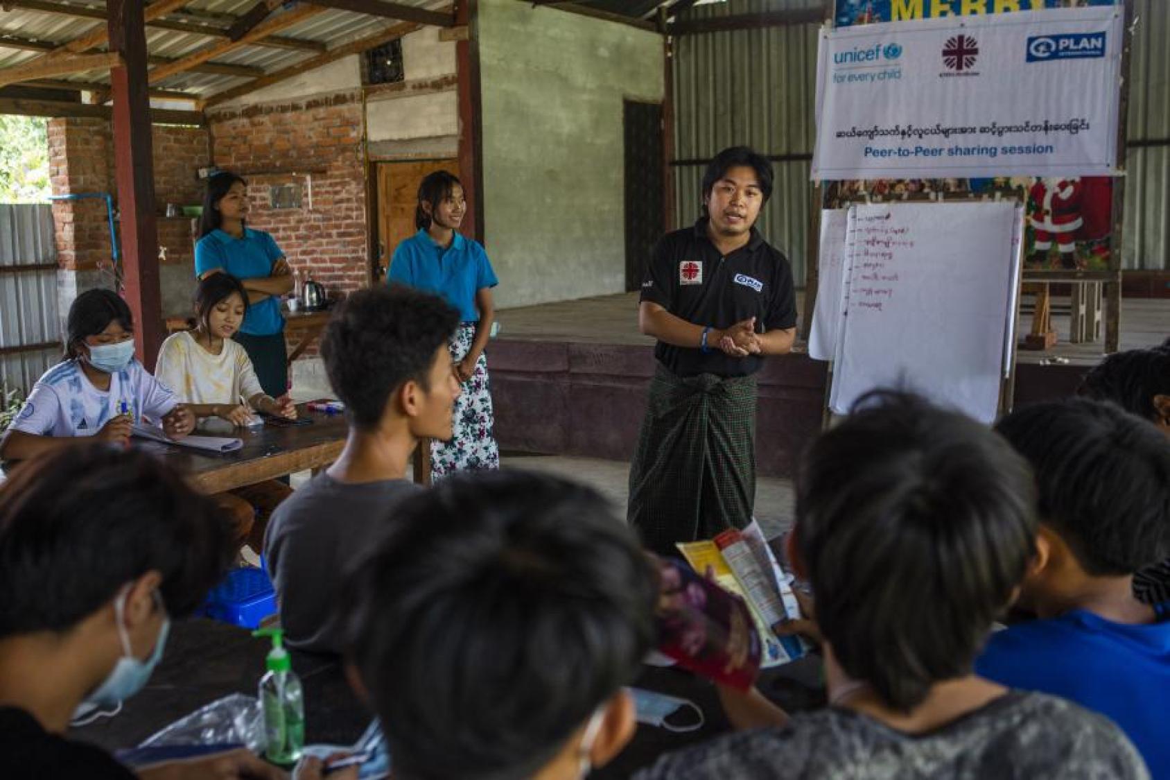 شاب يقف أمام بعض المراهقين، يتحدث إليهم في جلسة لتبادل المعارف بين الأقران.
