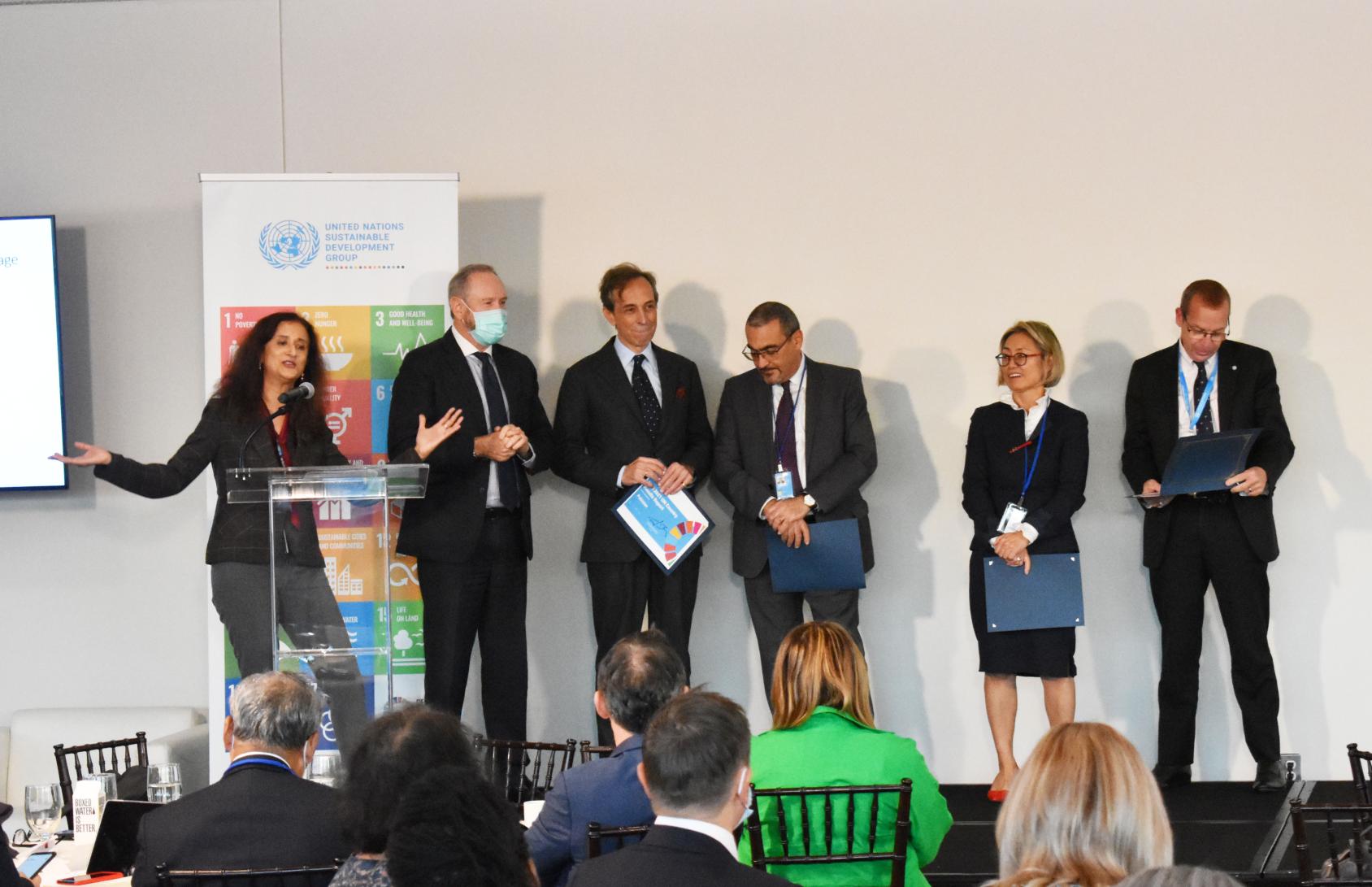 一名妇女站在讲台上，驻地协调员在她的两侧。