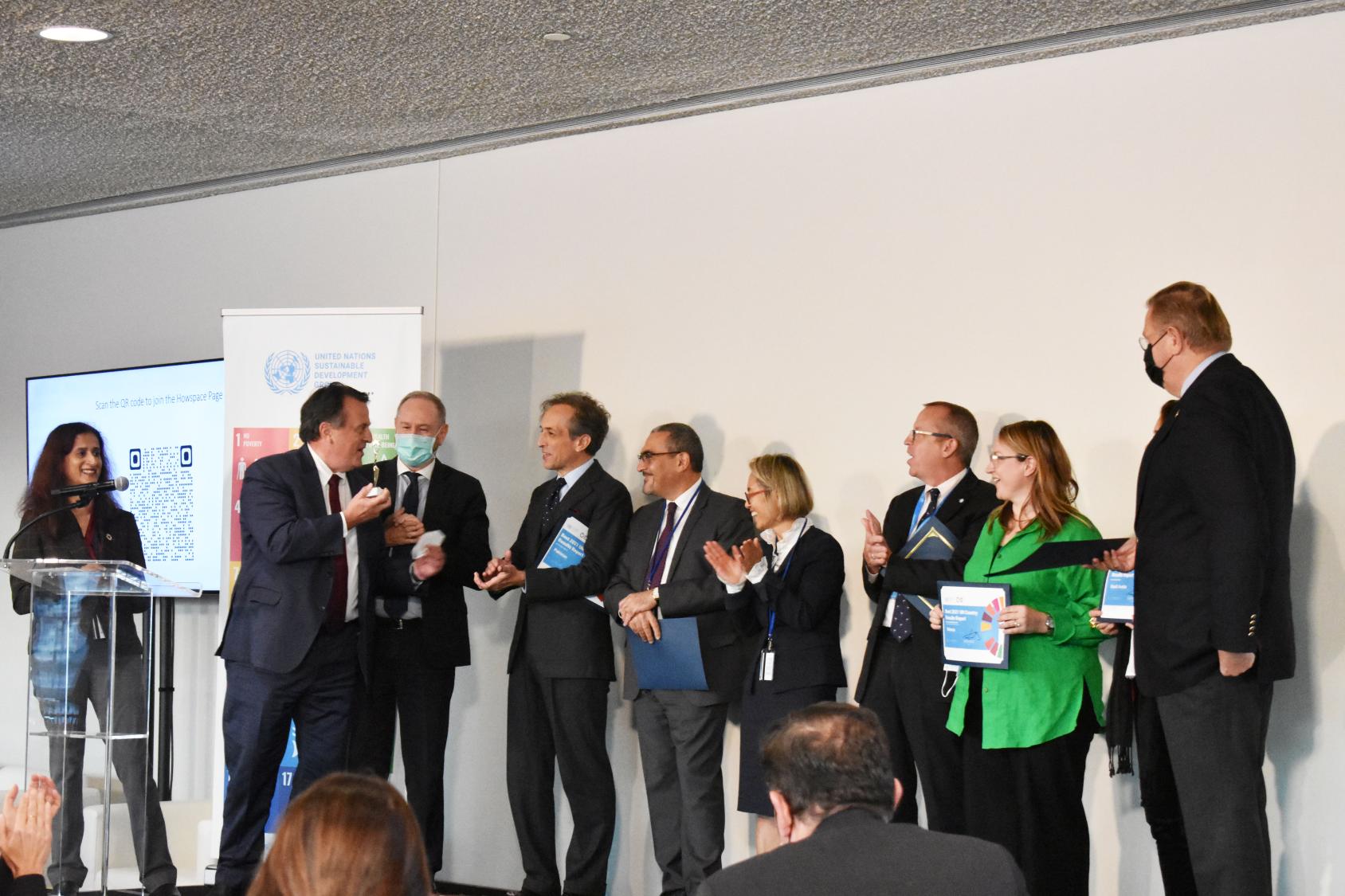 联合国官员站在舞台上，两个人靠在一起，在掌声中互相交谈。