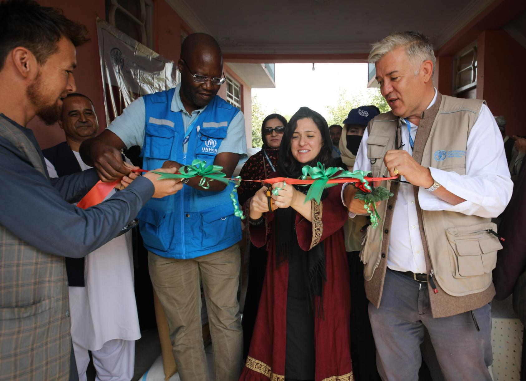 A woman using a scissor to cut a ribbon that is held by two men on her two sides. 