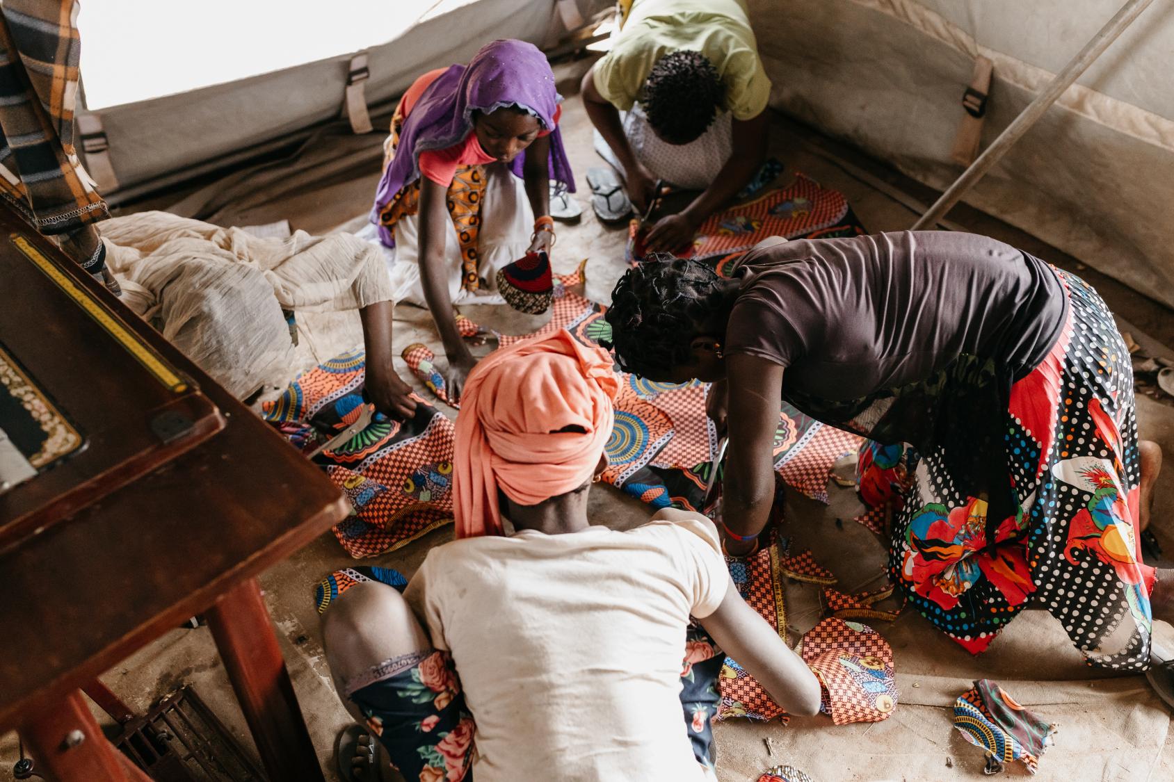 Five women crouched around the floor talking and working together