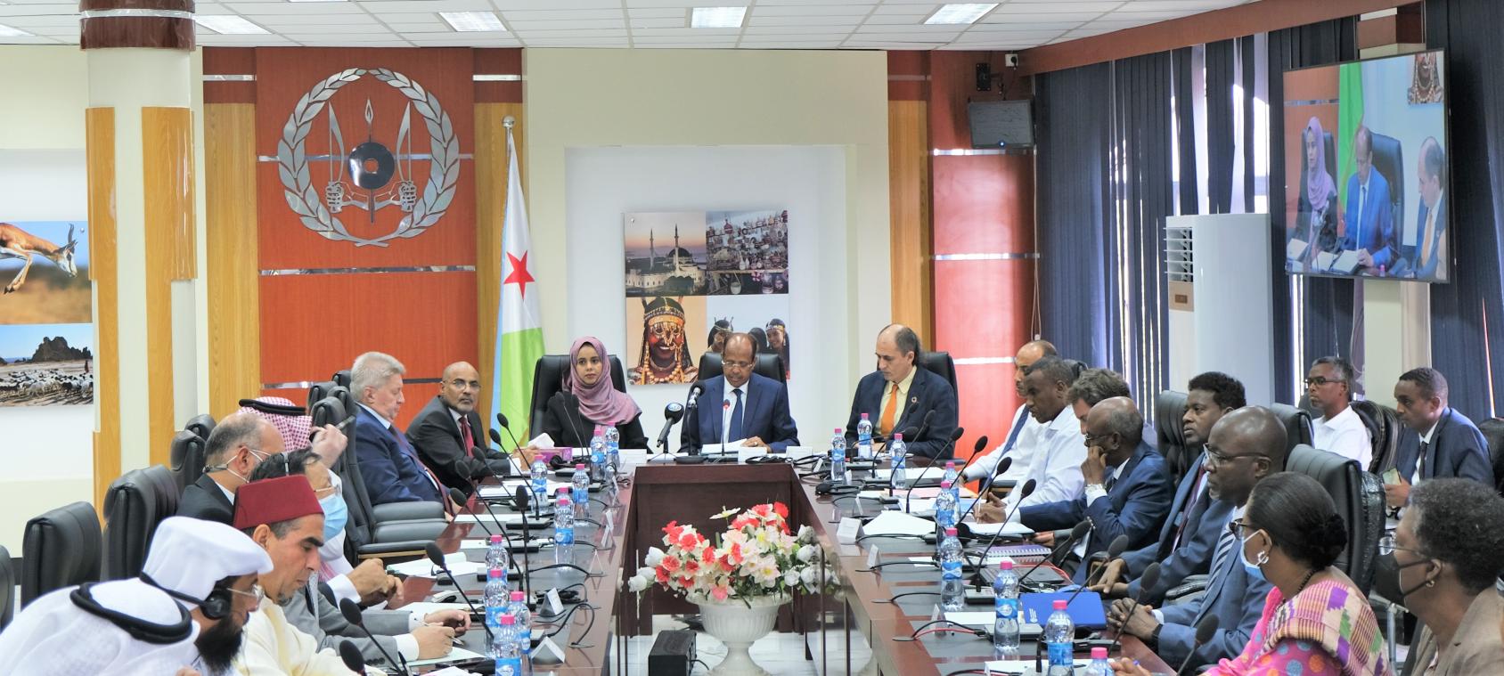 A group of people, in suits and formal dresses, gathered in a room with microphones on the desk