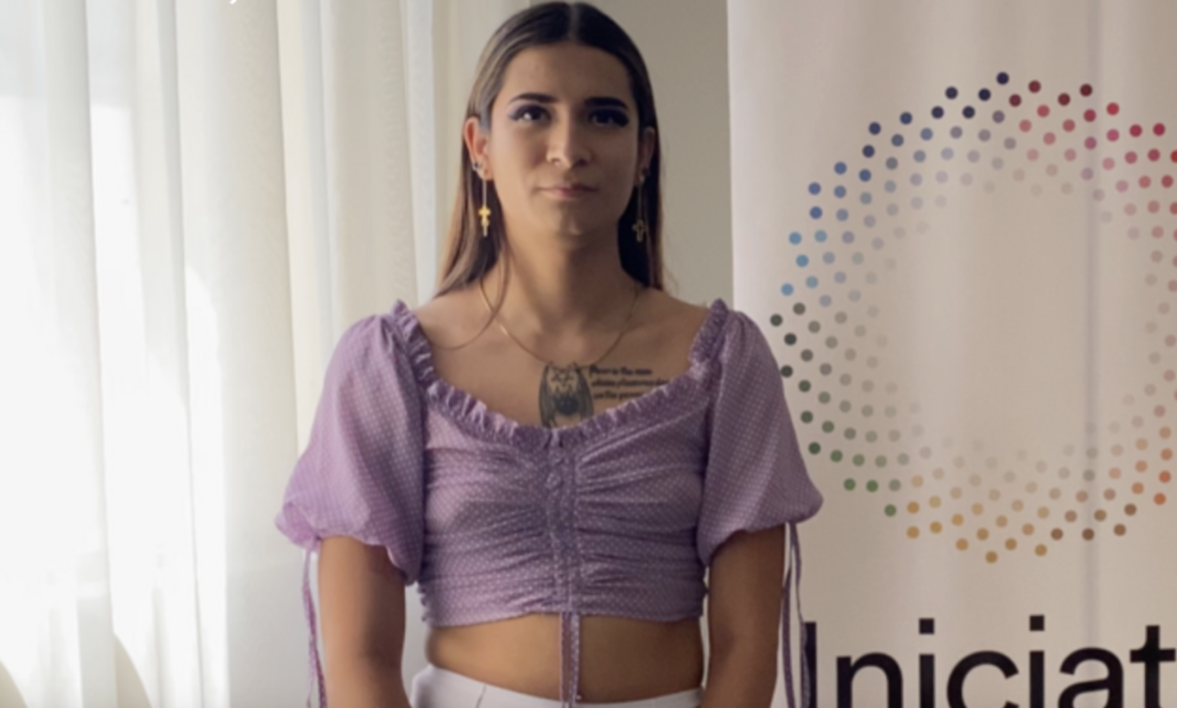 Person in a purple shirt stands in front of a white curtain
