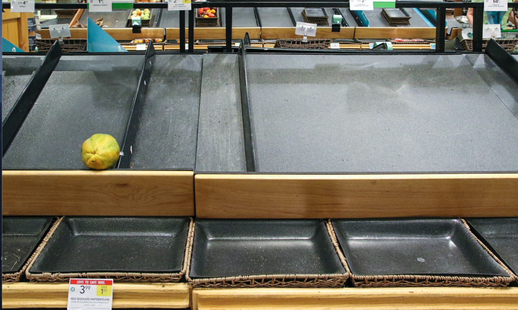 A single yellow fruit lies in an empty food produce shelf in a supermarket