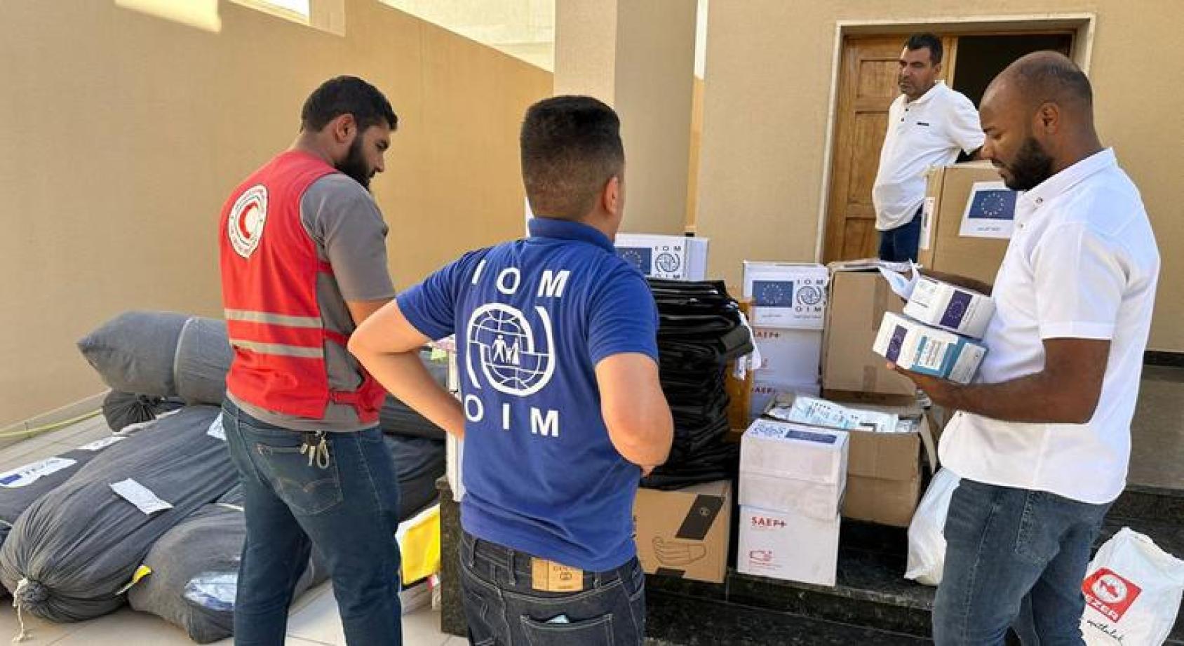 A group of men in IOM t-shirts and visibility vests look through boxes 