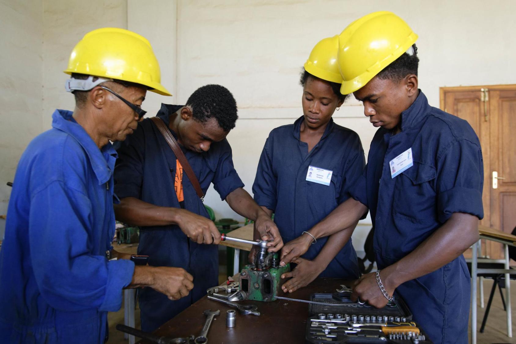 Four people in blue uniforms and yellow hardhats