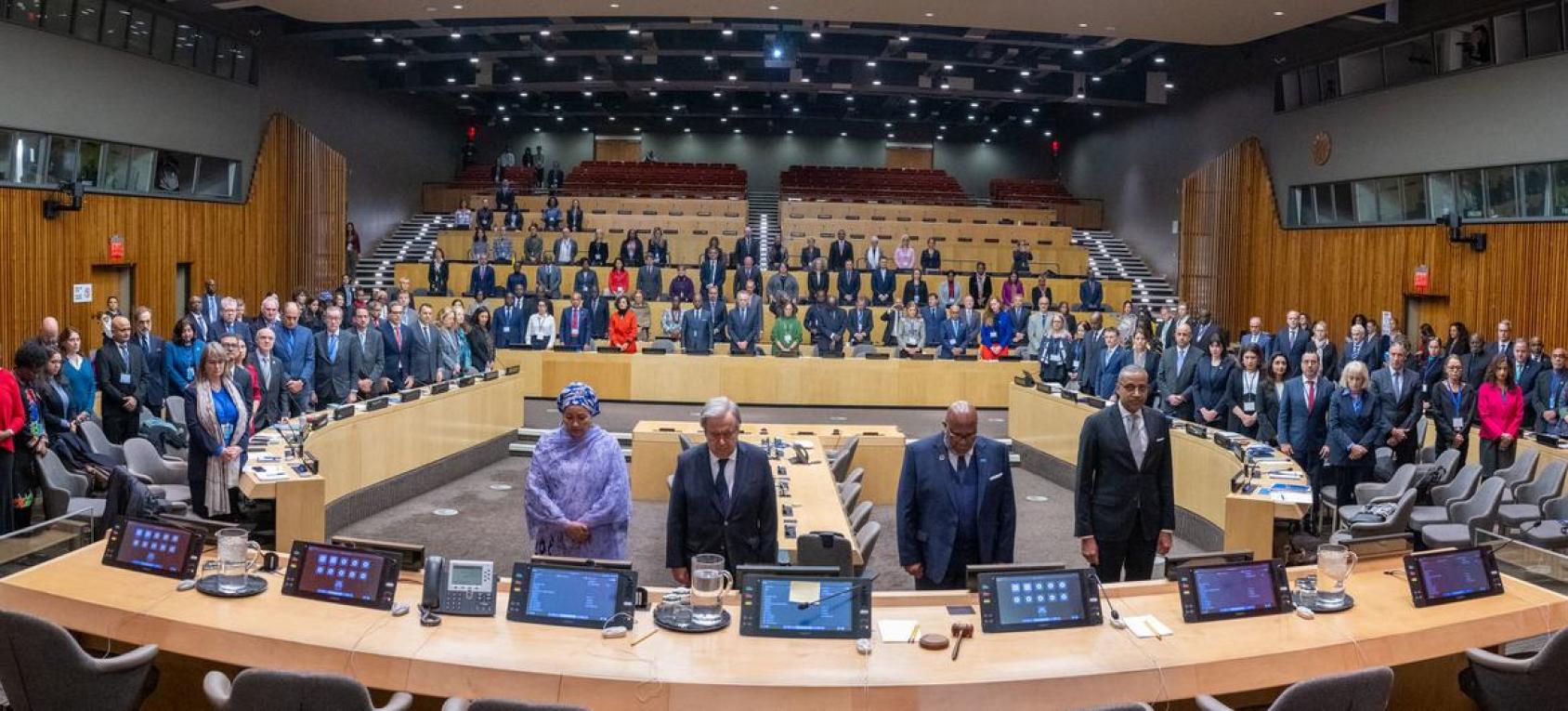 A group of people stand in silence in a circular room at the UN headquarters