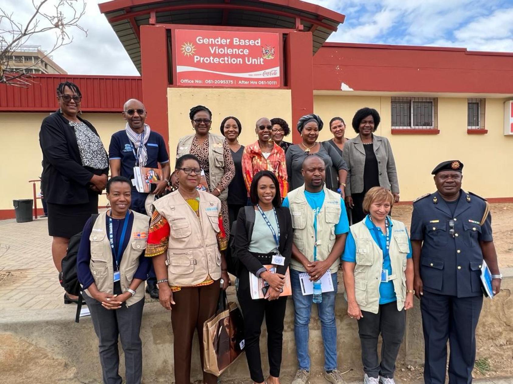 A group of fourteen people, standing in two rows, in front of a building that says "gender violence protection unit".