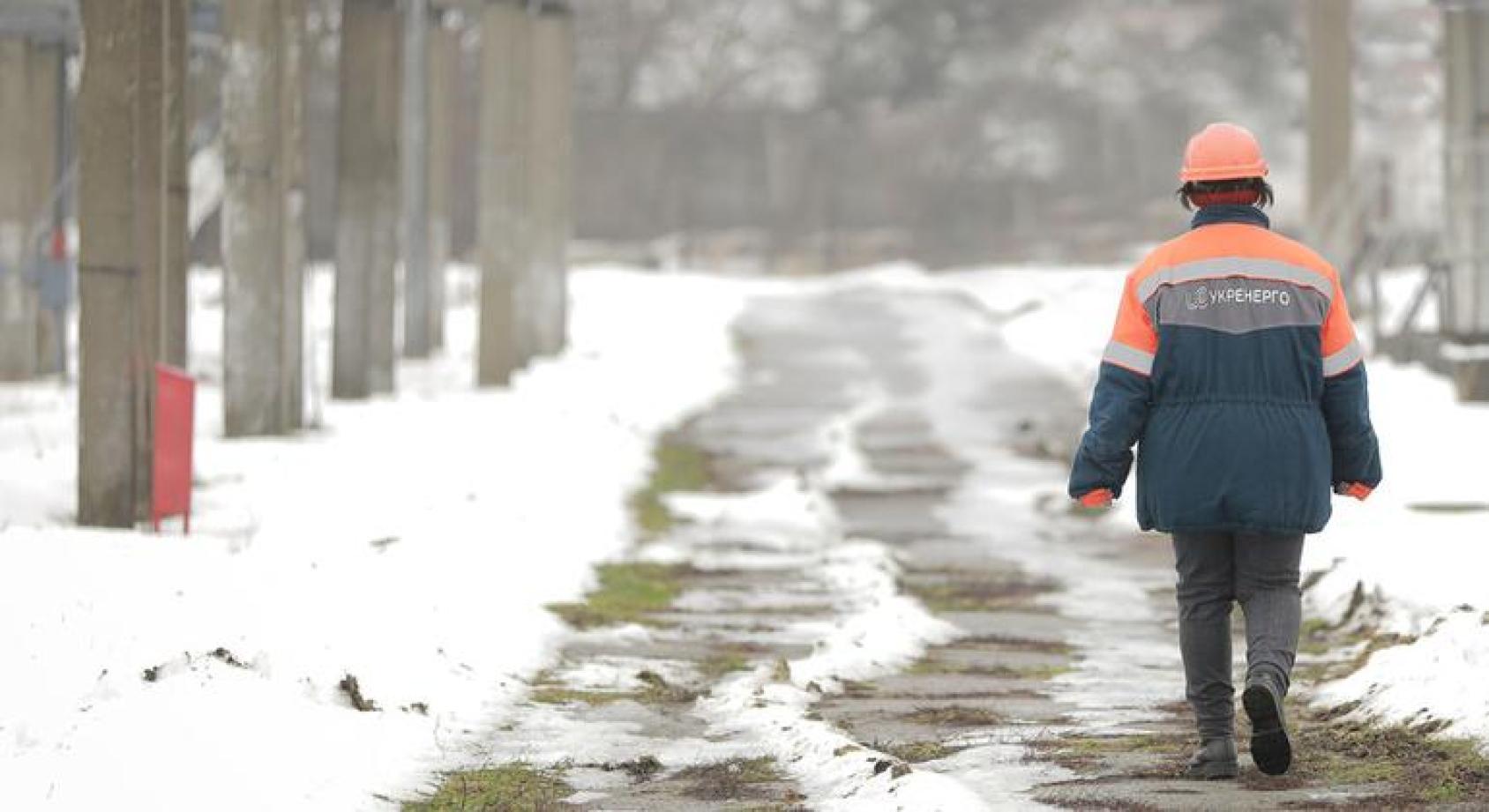 Человек в униформе сотрудника электростанции, сфотографирован со спины и идет по зимней аллее