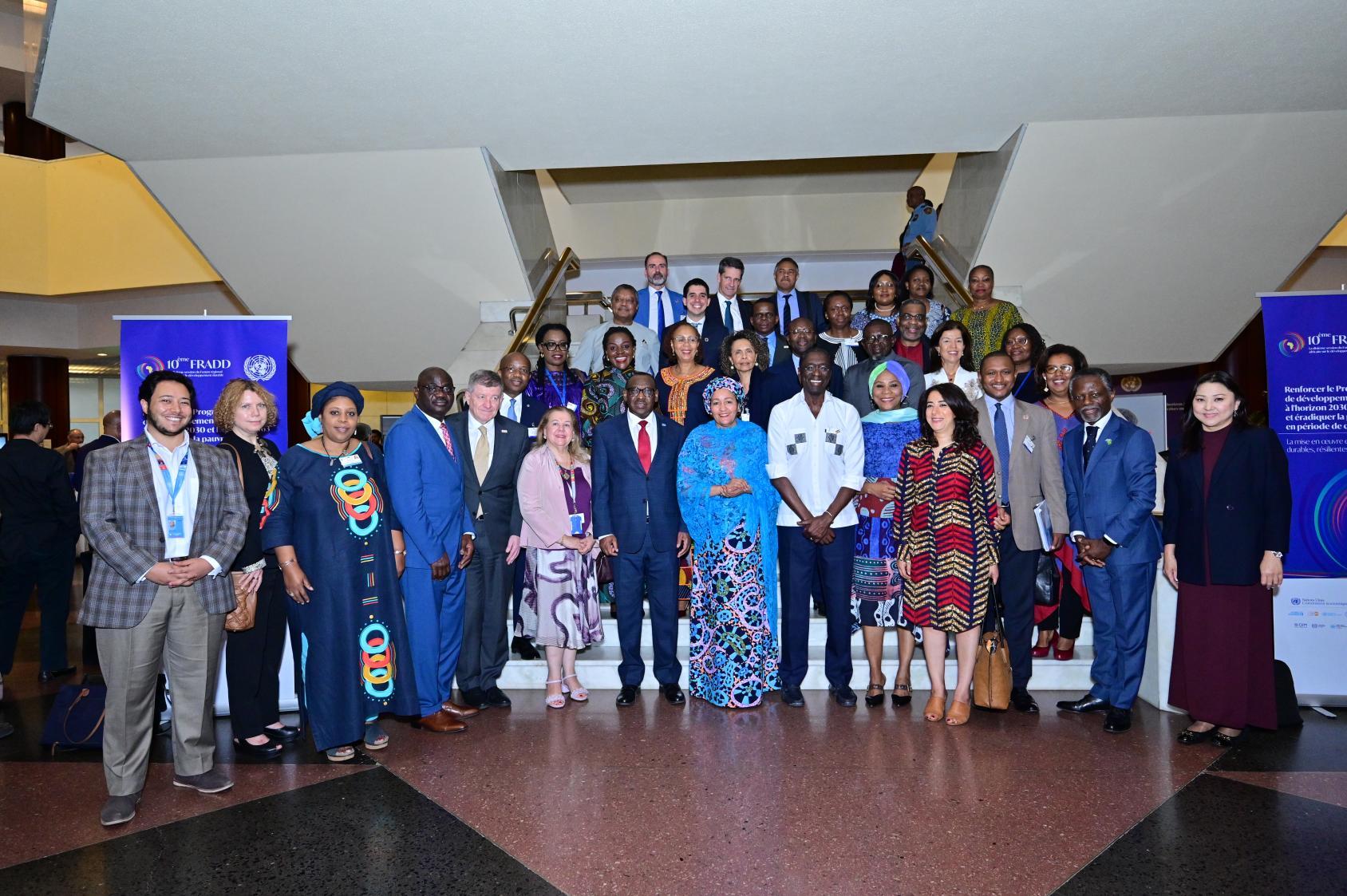 A group photo of several people in different coloured suits and dresses, standing in rows on a staircase