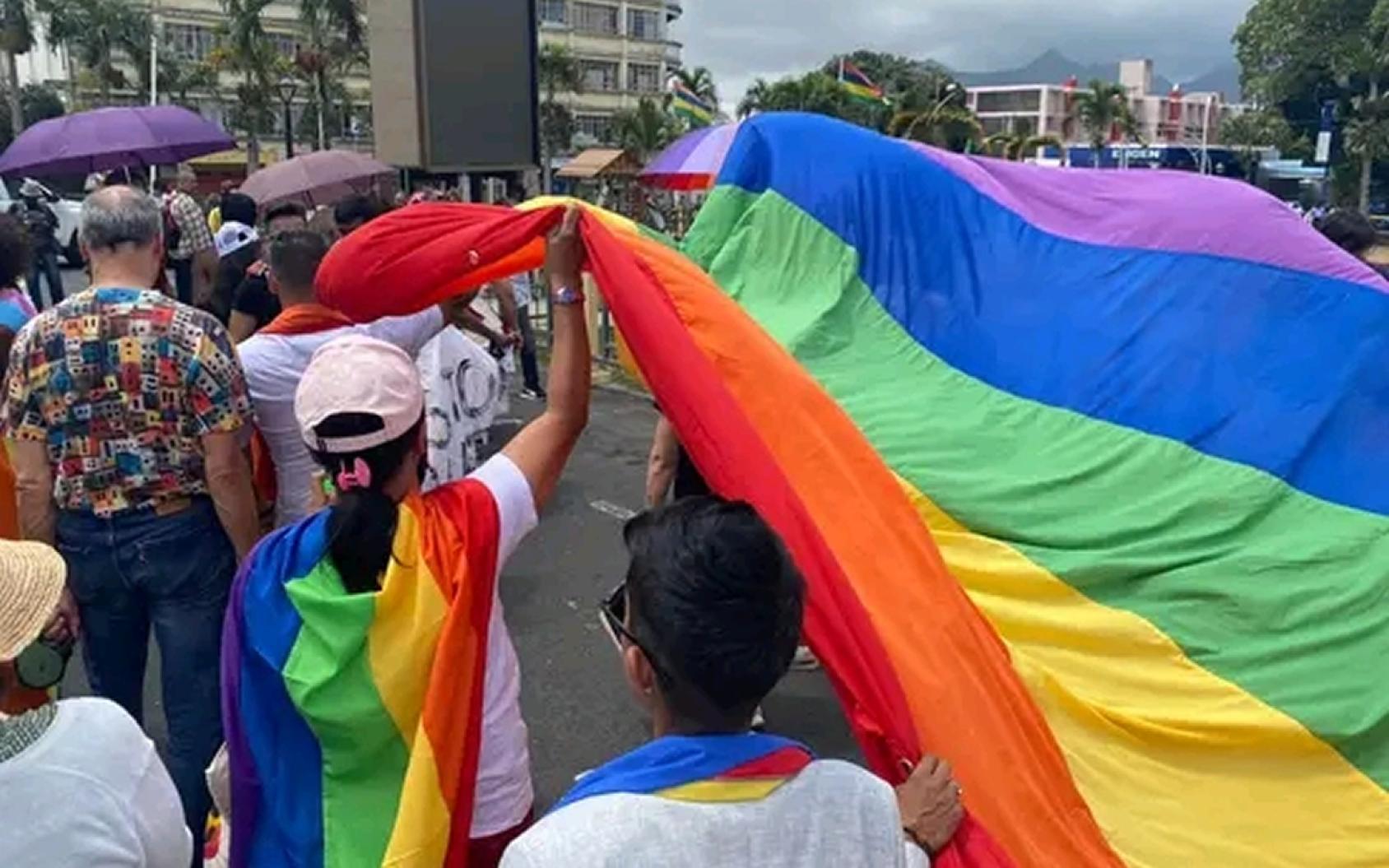 A group of people walking in on the street, holding up a rainbow flag