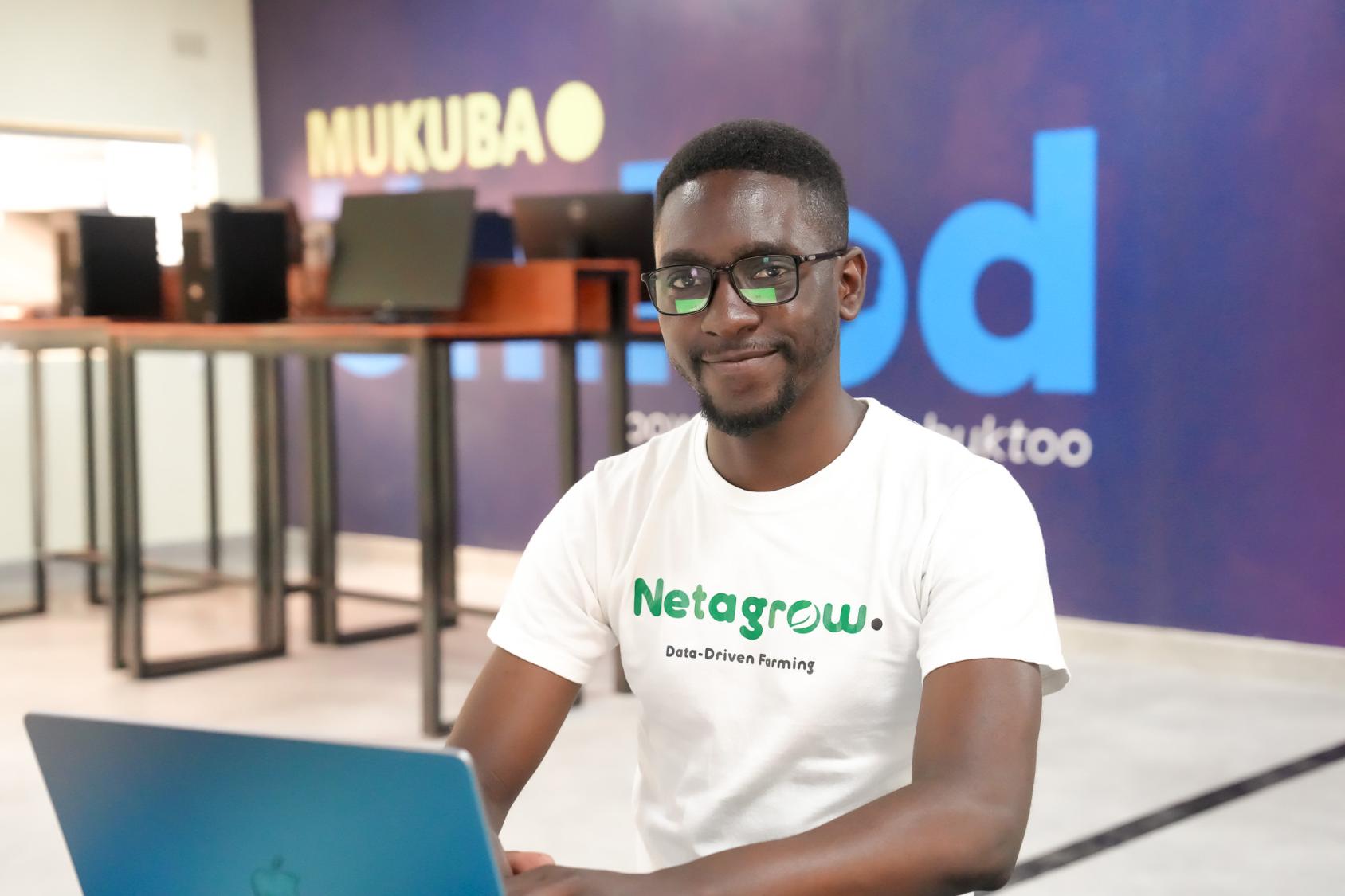 A man in a white shirt with black spectacles sits in front of a laptop in a swanky office