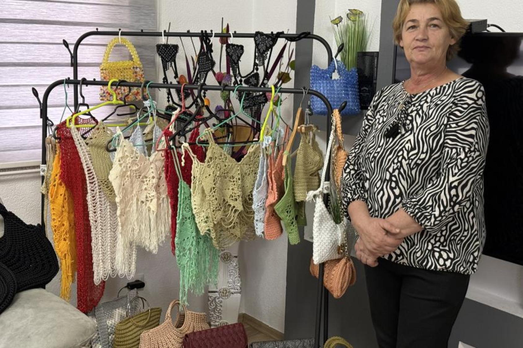 A woman in a printed black top stands in front of row of clothes