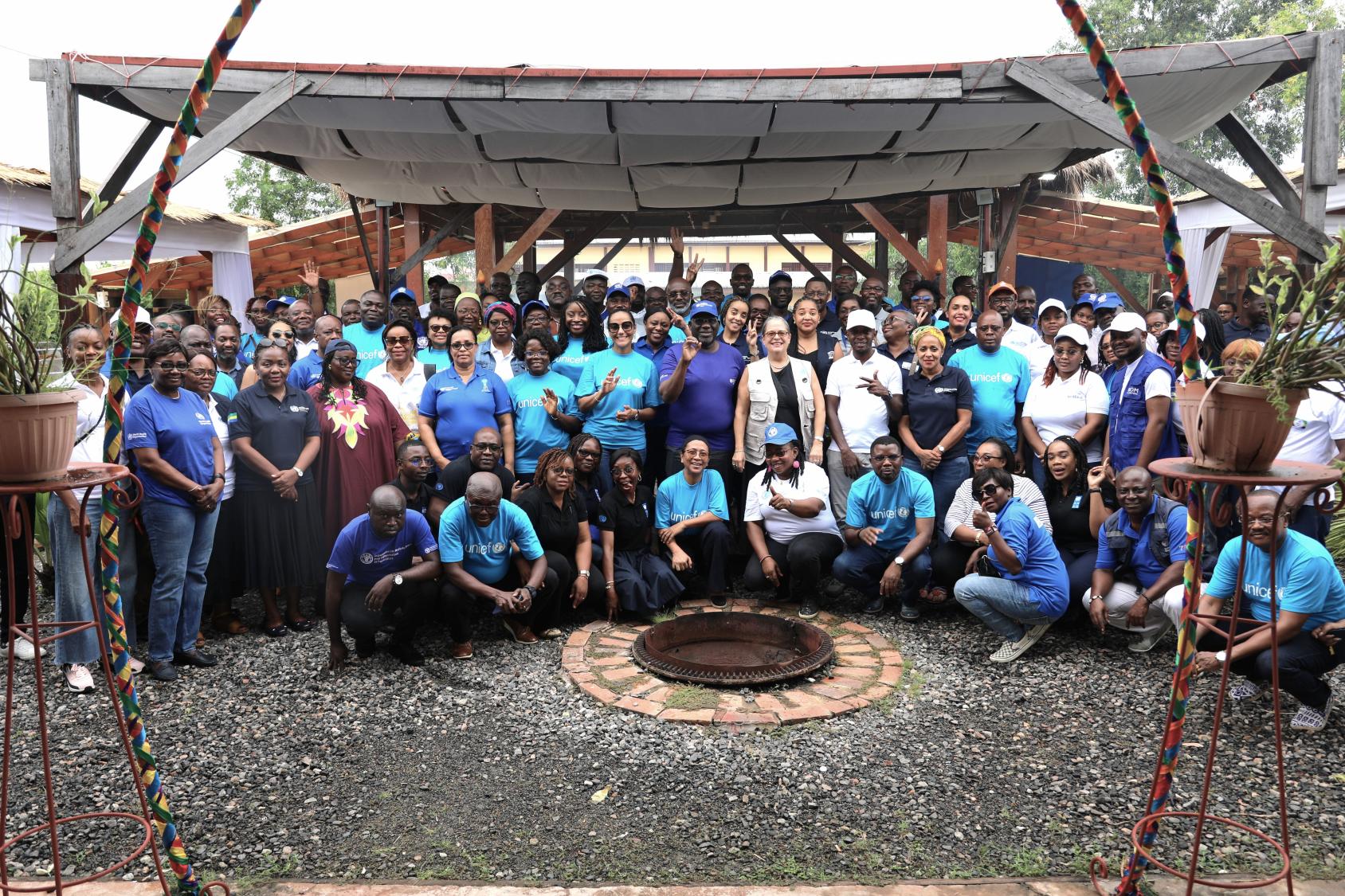A group of people in blue and purple shirts and caps gathered under an awning.