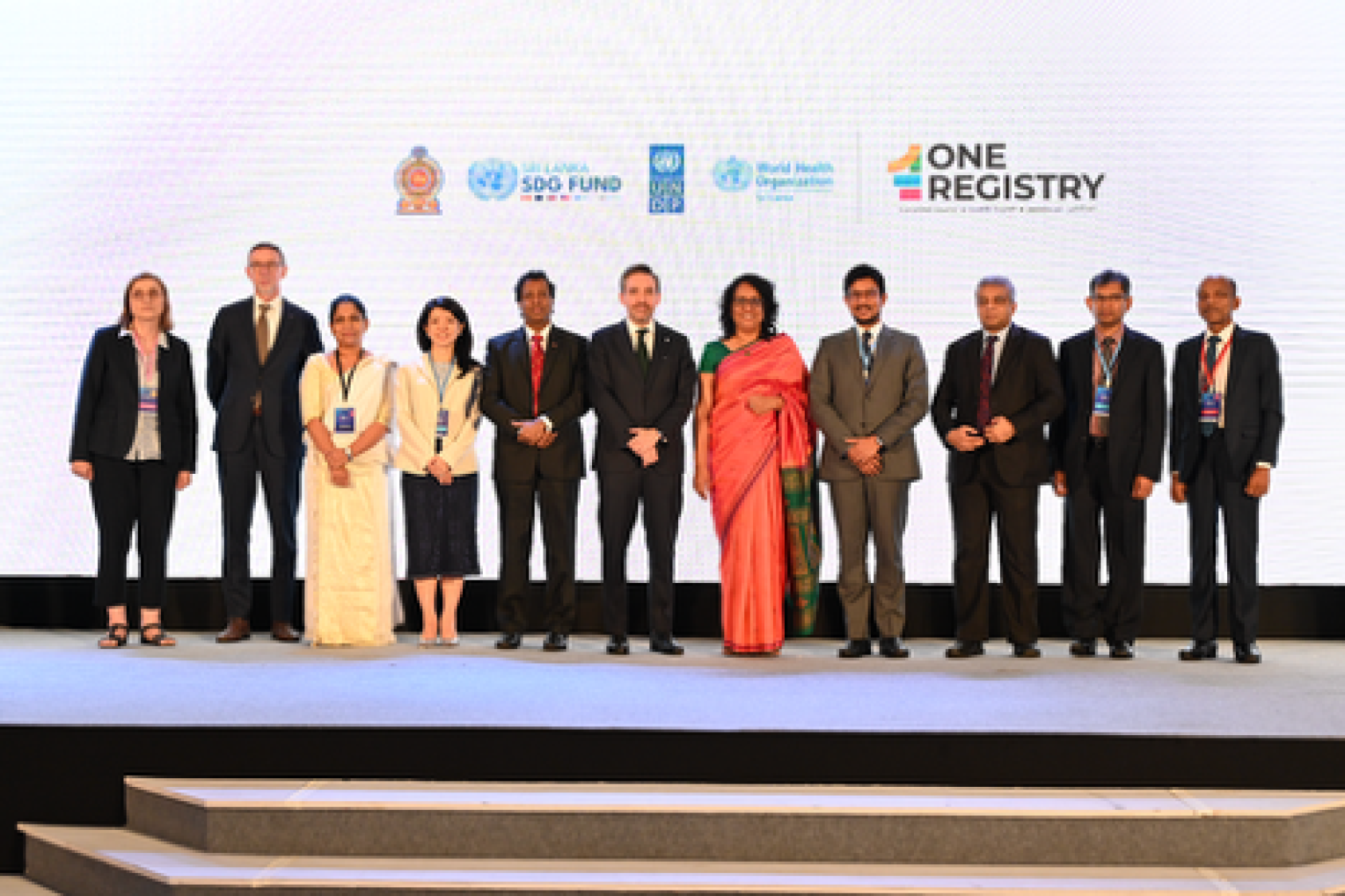 A group of eleven people in black suits and sarees at a launch event