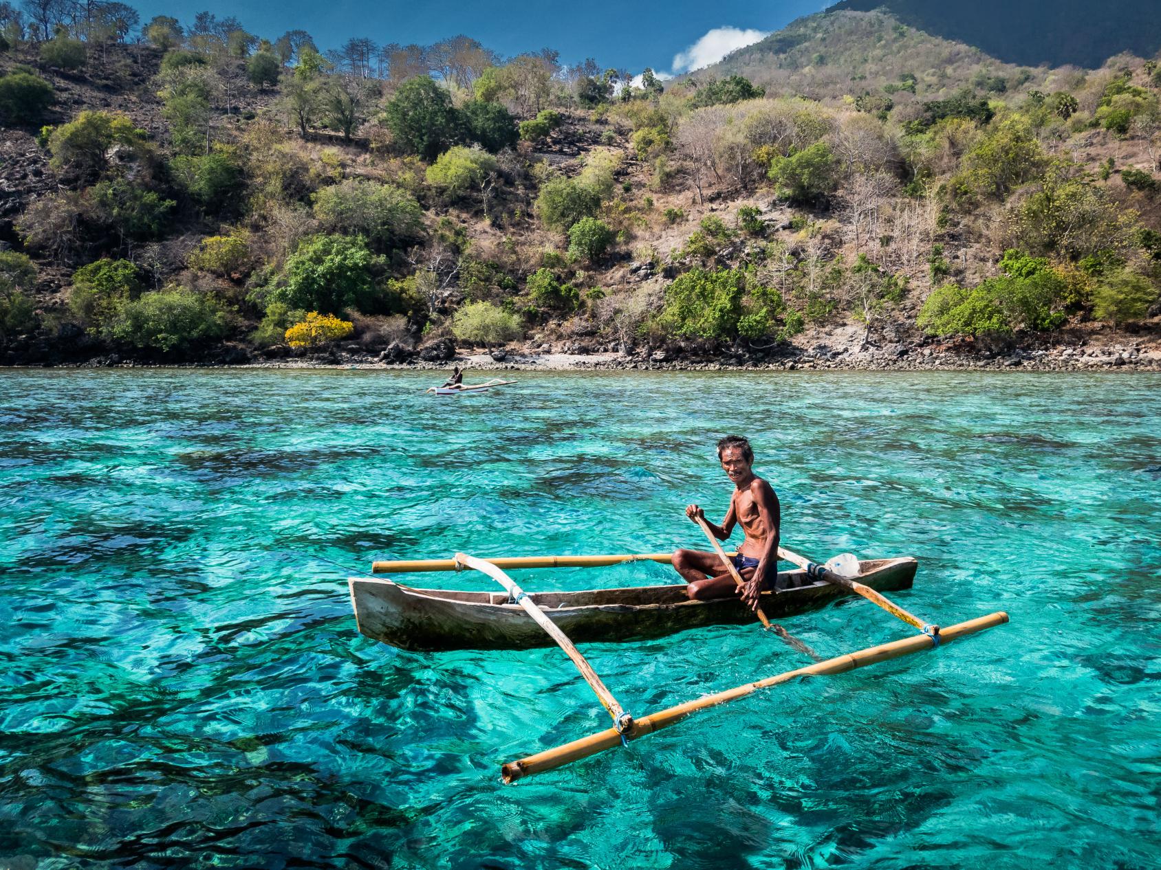 A man in a makeshift boat sails in a blue lagoon