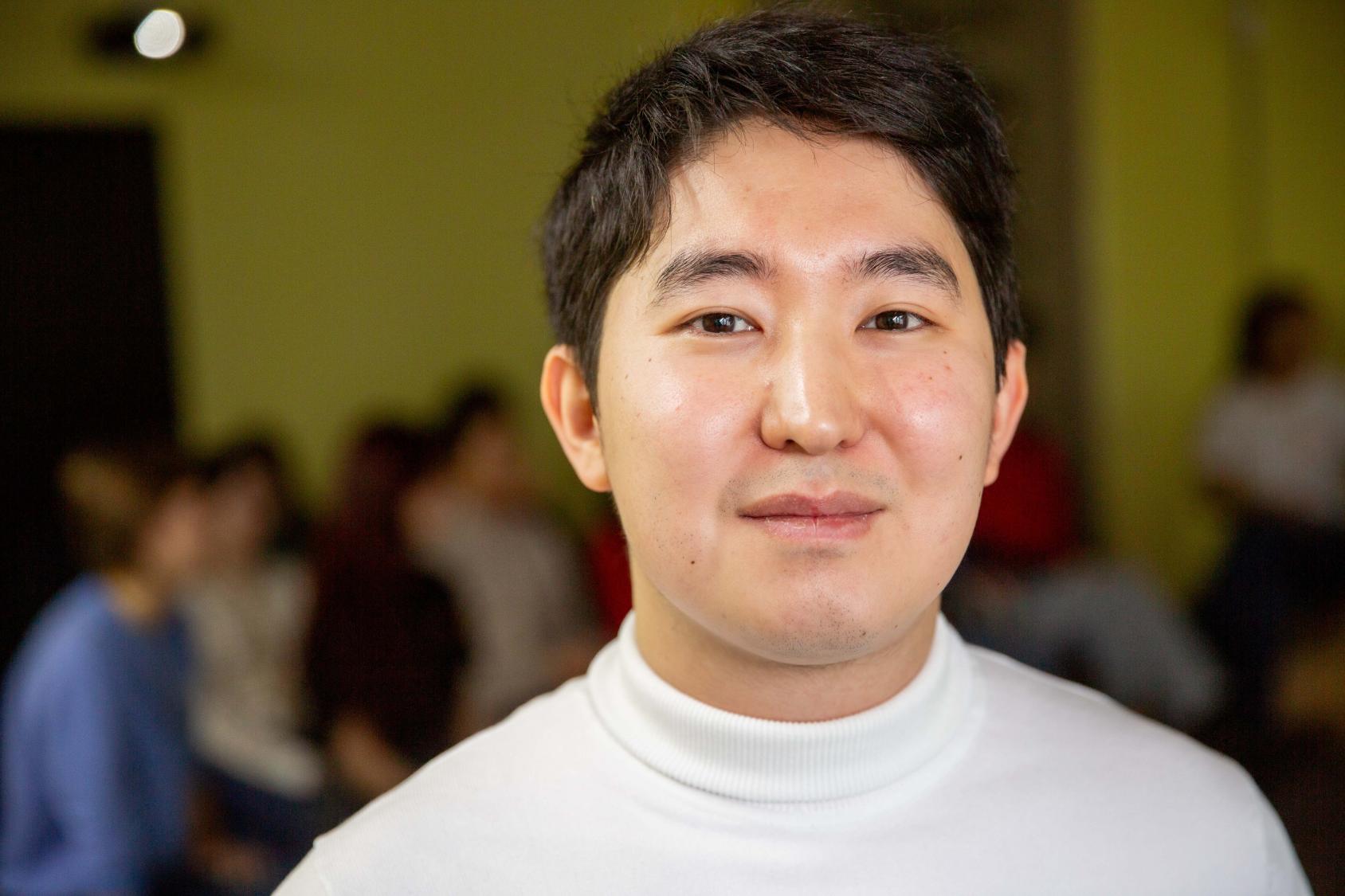 Мужчина в белой водолазке смотрит в камеру и улыбается