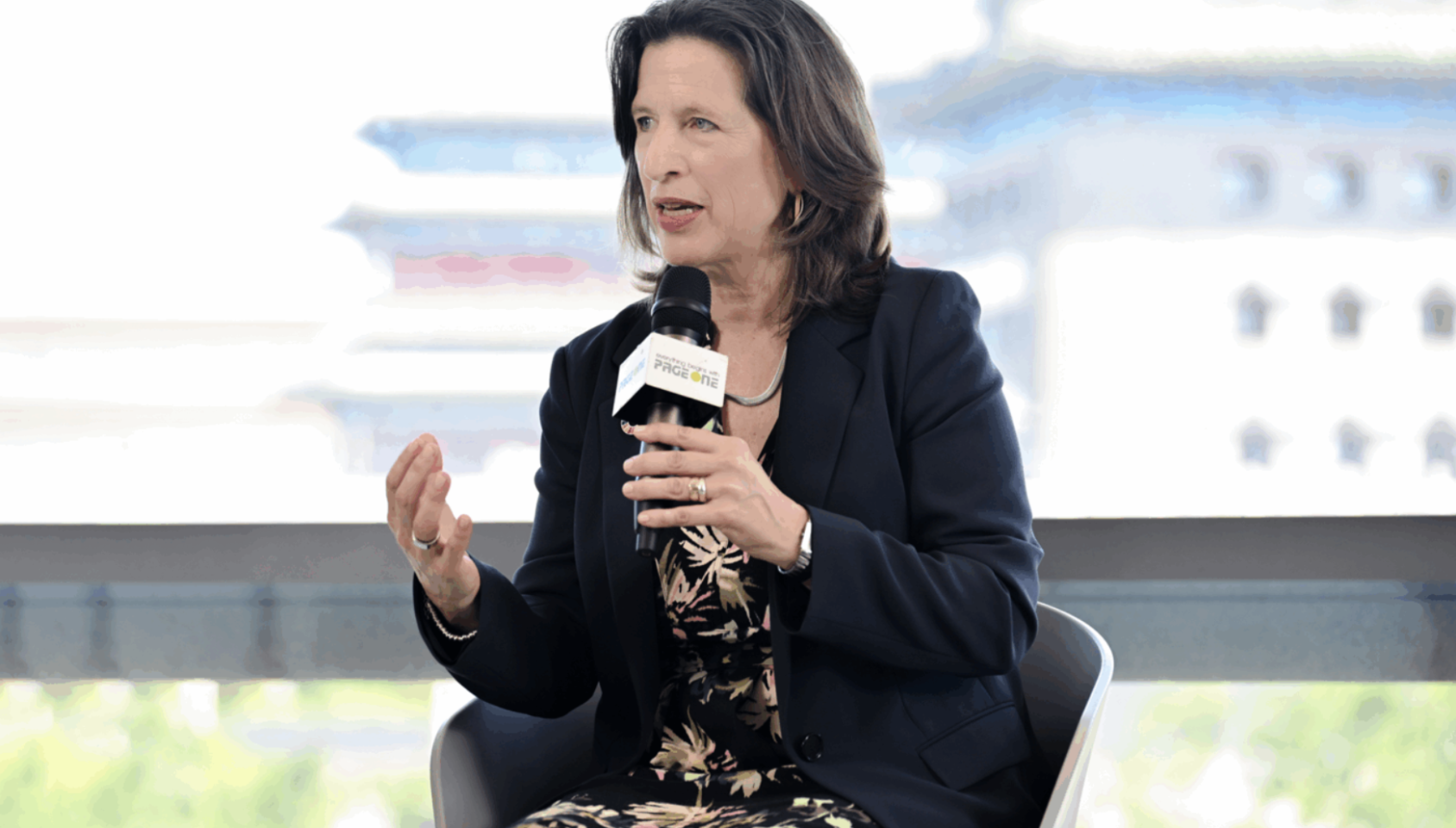 一位身穿黑色外套的中短发女性拿着话筒坐着发言