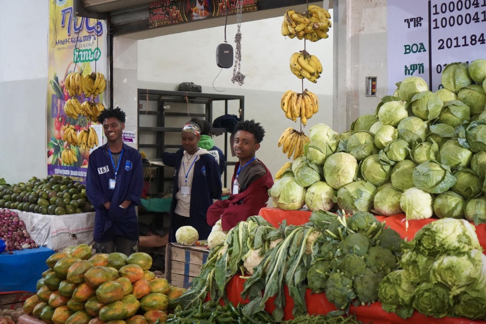 A vegetable market with two boys looking at the screen
