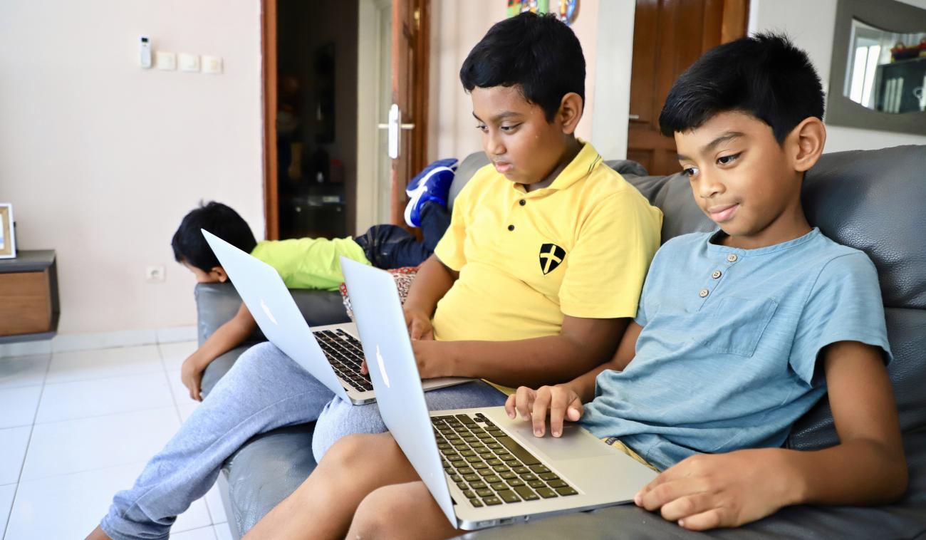 Deux jeunes garçons sont assis dans un canapé, chacun devant son ordinateur portable.