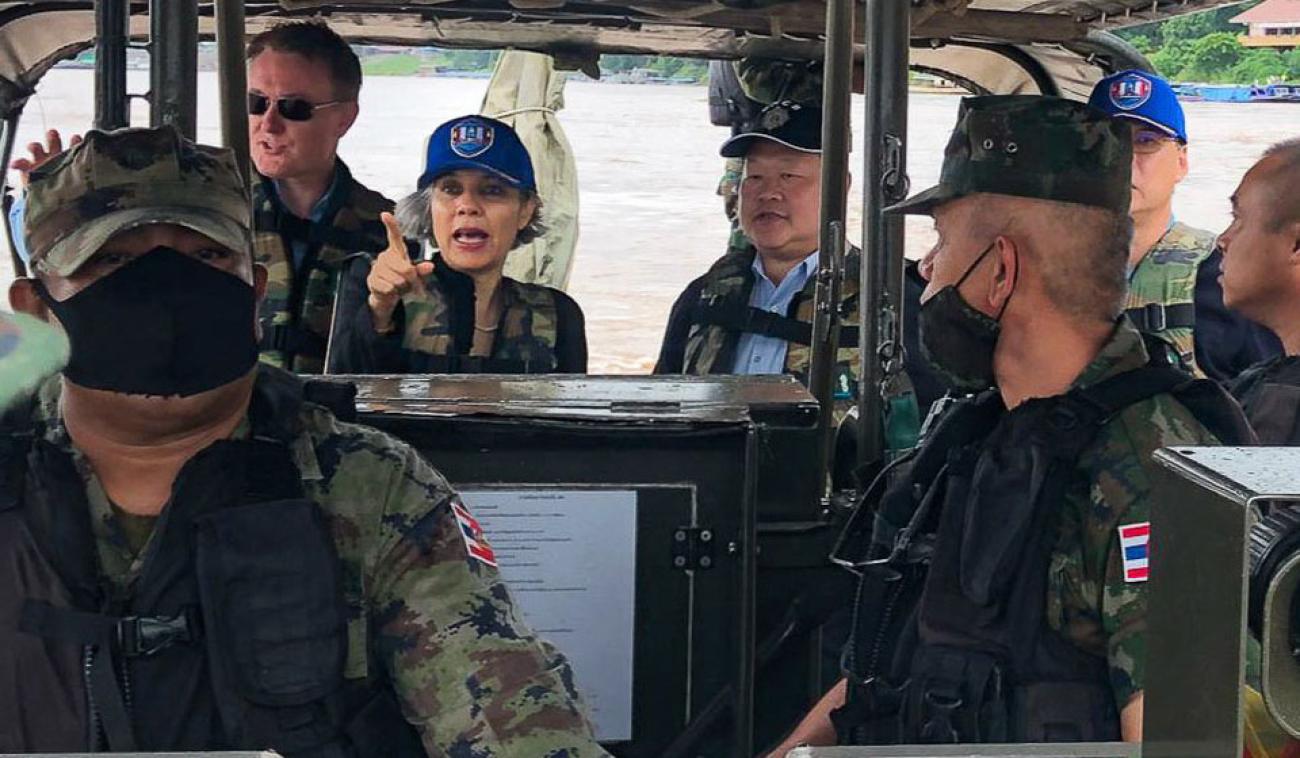 La Coordinadora Residente de la ONU en Tailandia, Gita Sabharwal (al fondo del centro) da indicaciones a miembros de una patrulla, en el río Mekong. Todos los presentes llevan puesta indumentaria oscura, y chaleco con camuflaje.