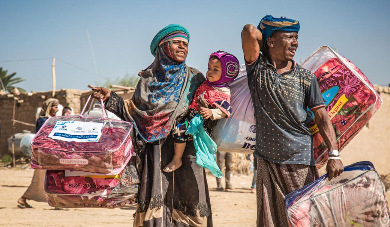 A displaced family in Marib, Yemen, carries a winter aid package back to their shelter.