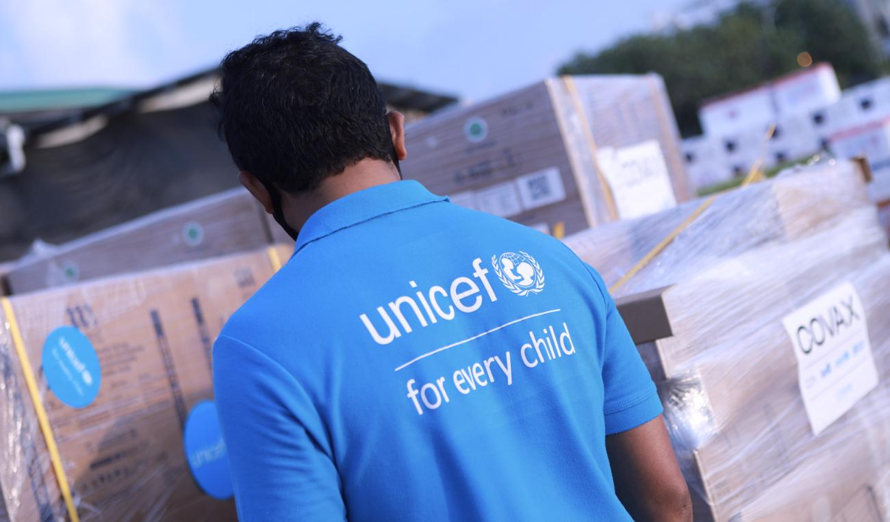 A man wearing a light blue UNICEF shirt looks over the delivery of vaccines wrapped in wrapping paper.