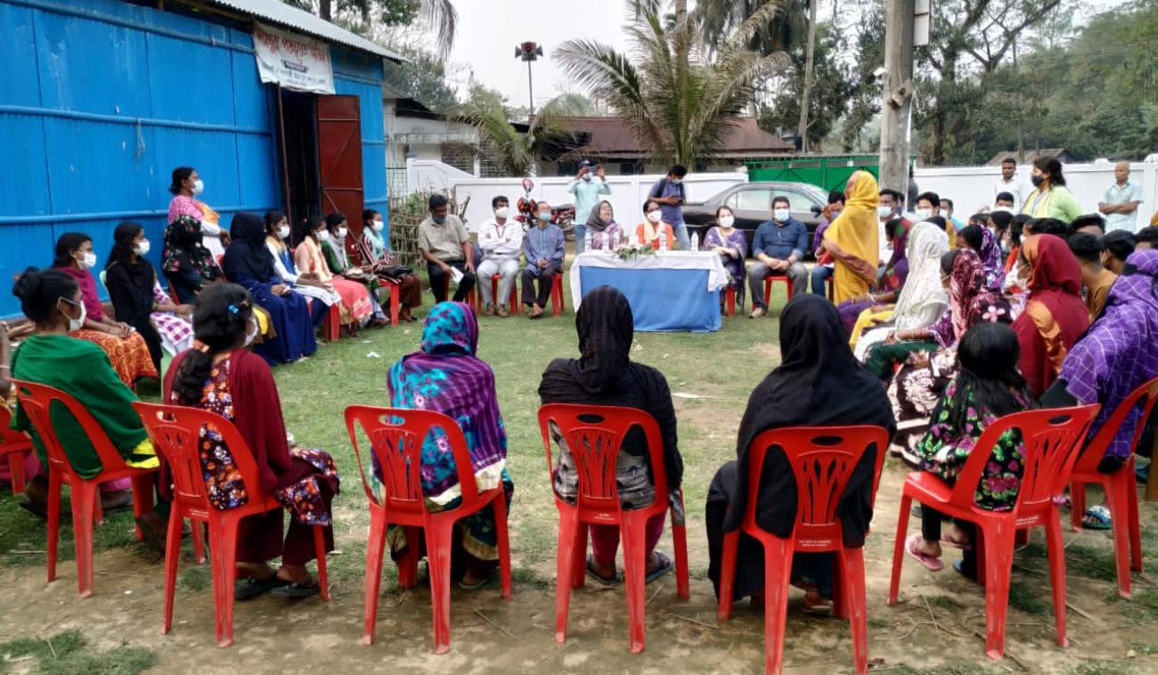 تجلس مجموعة كبيرة من الأشخاص يرتدون كمامات في دائرة ويتحدث شخص واحد في الوسط.